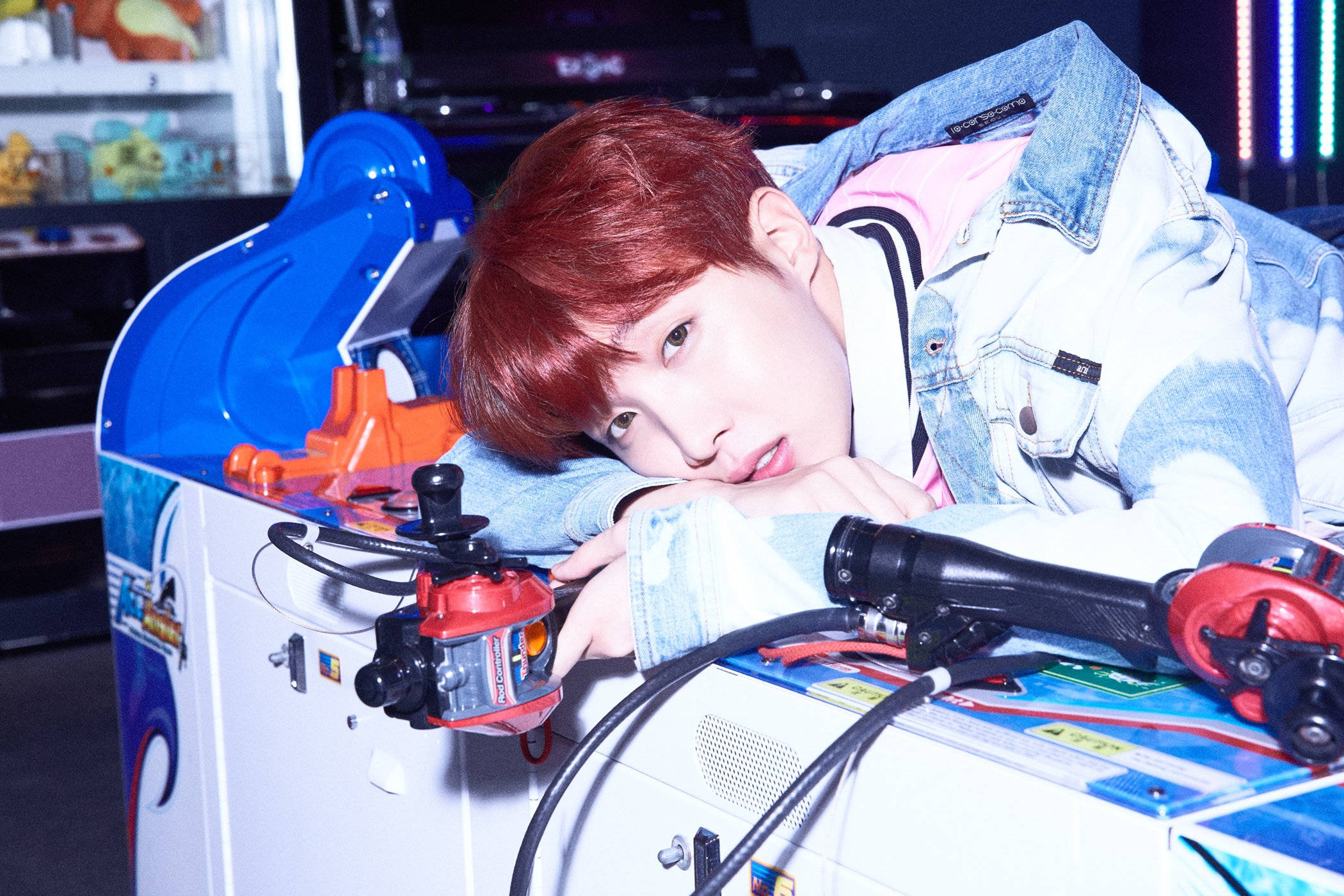 j-hope 桌布 壁紙 — 一位紅髮年輕男子在昏暗的遊戲室裡俯身於色彩繽紛的街機上。