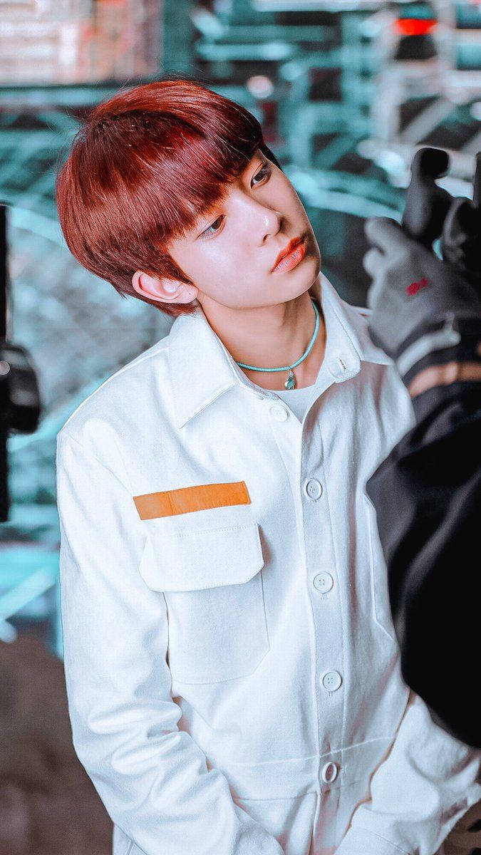 Kpop Aesthetic 桌布 壁紙 — 一位紅髮年輕男子穿著帶有橙色補丁的白色外套，在模糊的城市環境中向上看。