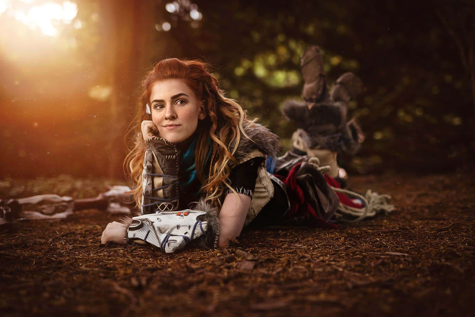 Gaming Cosplay 桌布 壁紙 — 一位紅髮戰士穿著毛皮鑲邊的盔甲躺在森林地面上，沐浴在金黃色的日落光線中，背景是散景的樹葉。
