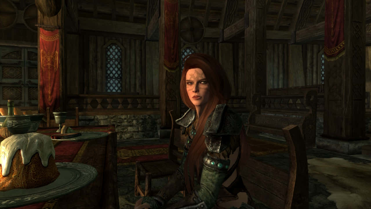 Aela The Huntress 桌布 壁紙 — 一位紅髮戰士身穿盔甲，坐在光線昏暗的中世紀大廳的木桌旁，周圍有旗幟和蛋糕。