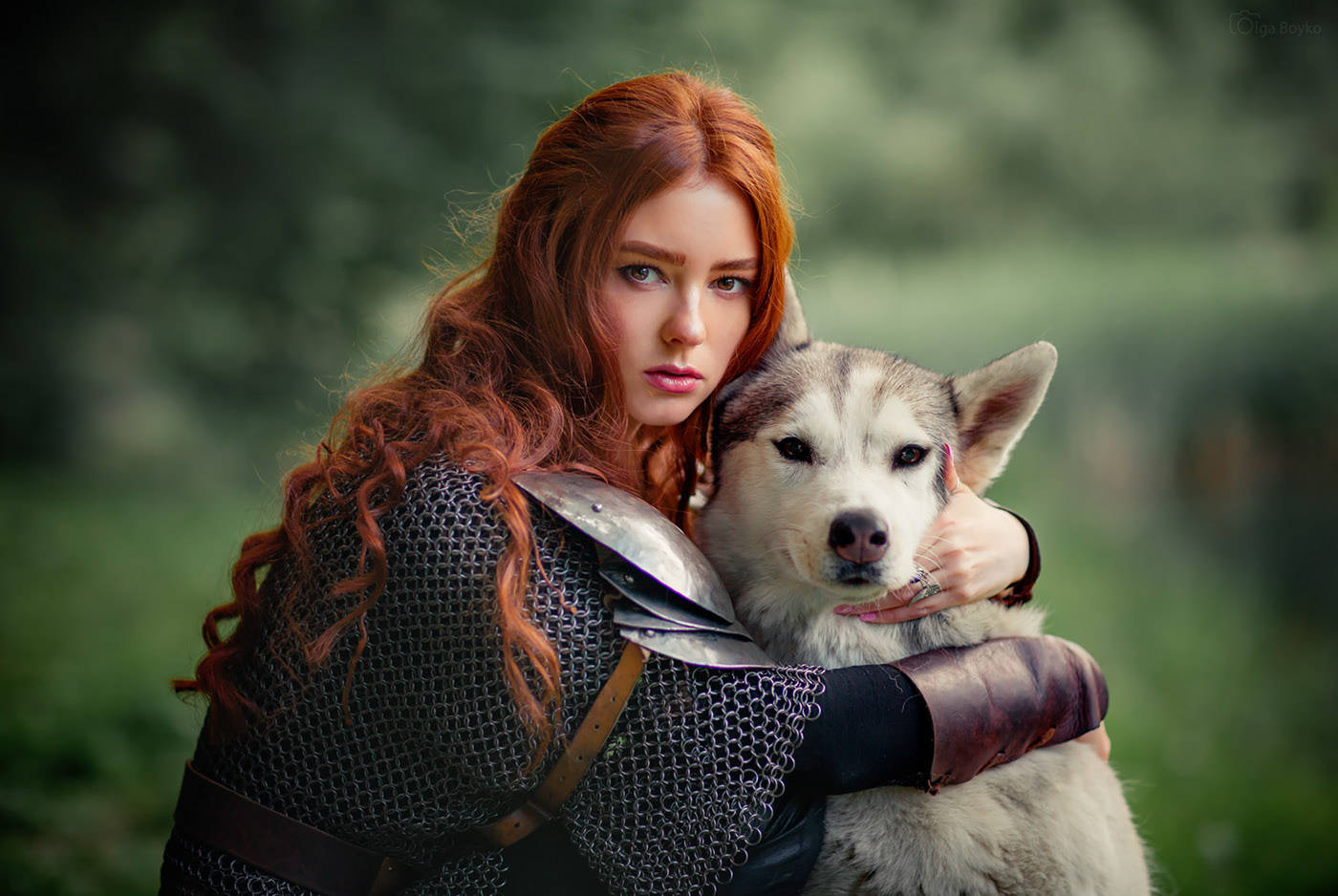 Dog And Girl 桌布 壁紙 — 一位紅髮戰士身穿鎖子甲，在柔和的綠色森林背景下輕輕抱著一隻哈士奇狗。