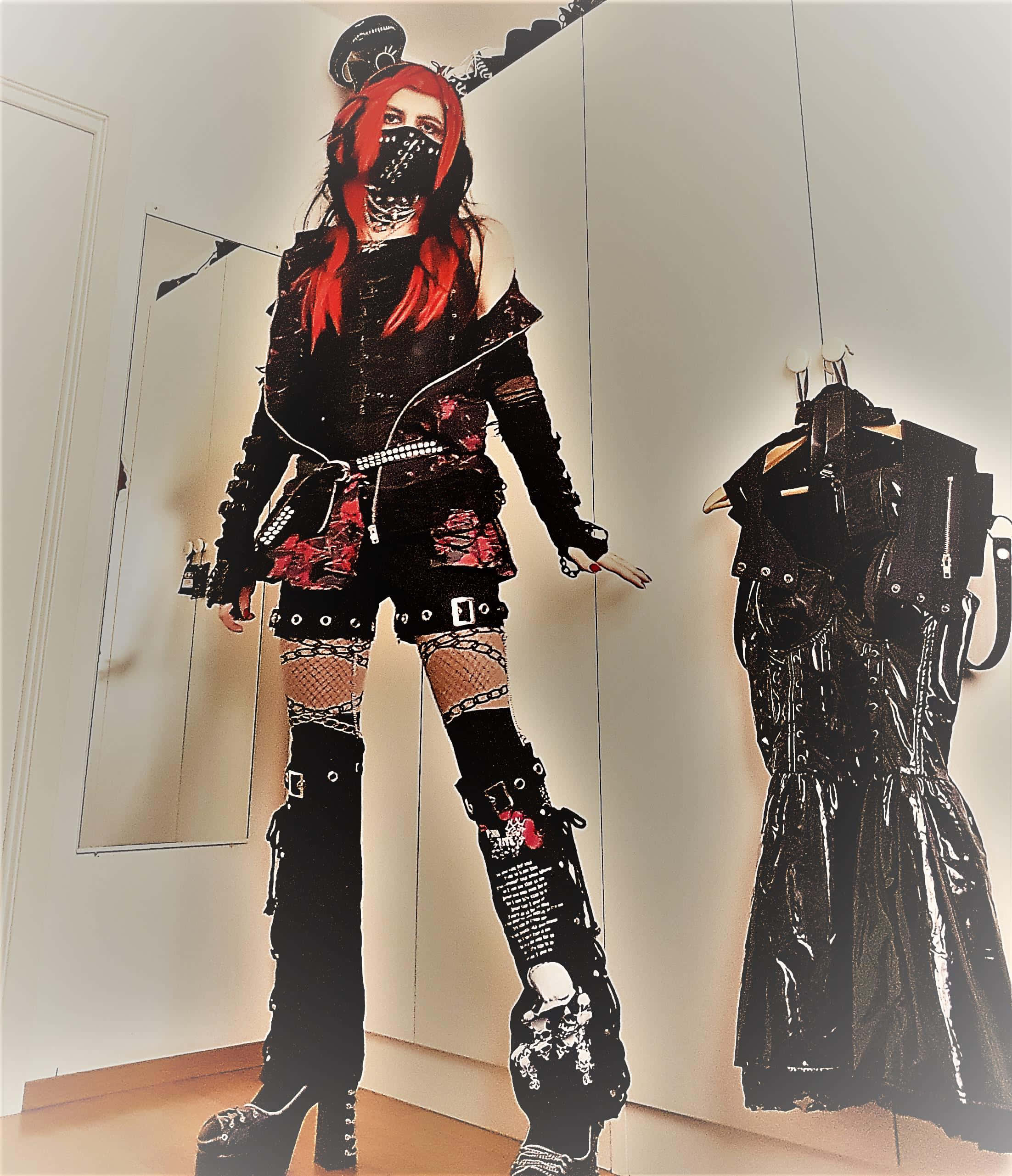 Visual Kei 桌布 壁紙 — 一位紅髮戴著口罩的人，身穿黑色龐克裝束，搭配魚網襪和鉚釘靴，旁邊掛著一件相配的外套。