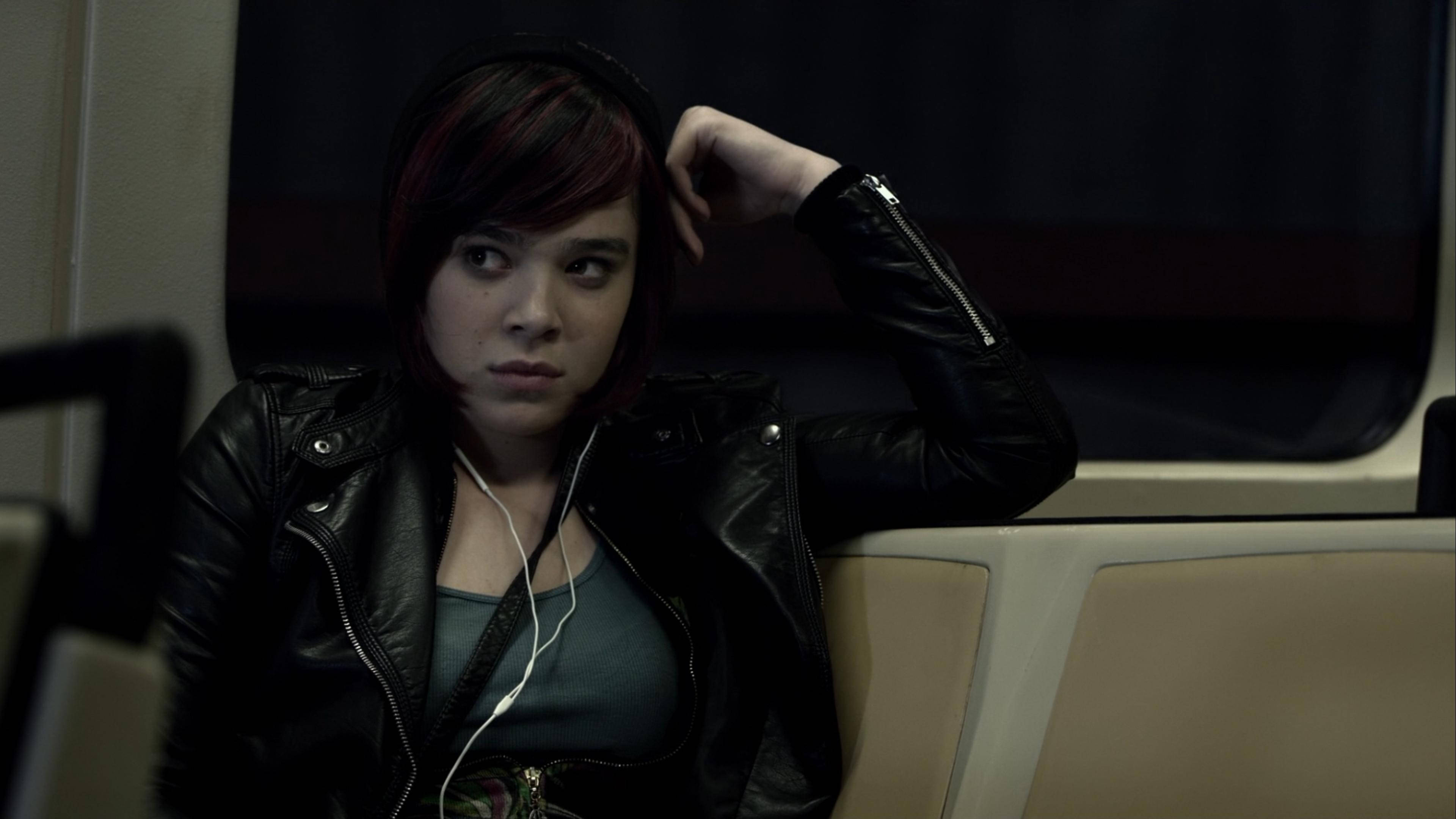 Hailee Steinfeld 桌布 壁紙 — 一位紅髮挑染的年輕女性，穿著黑色皮夾克和白色耳機，若有所思地坐在捷運座位上。