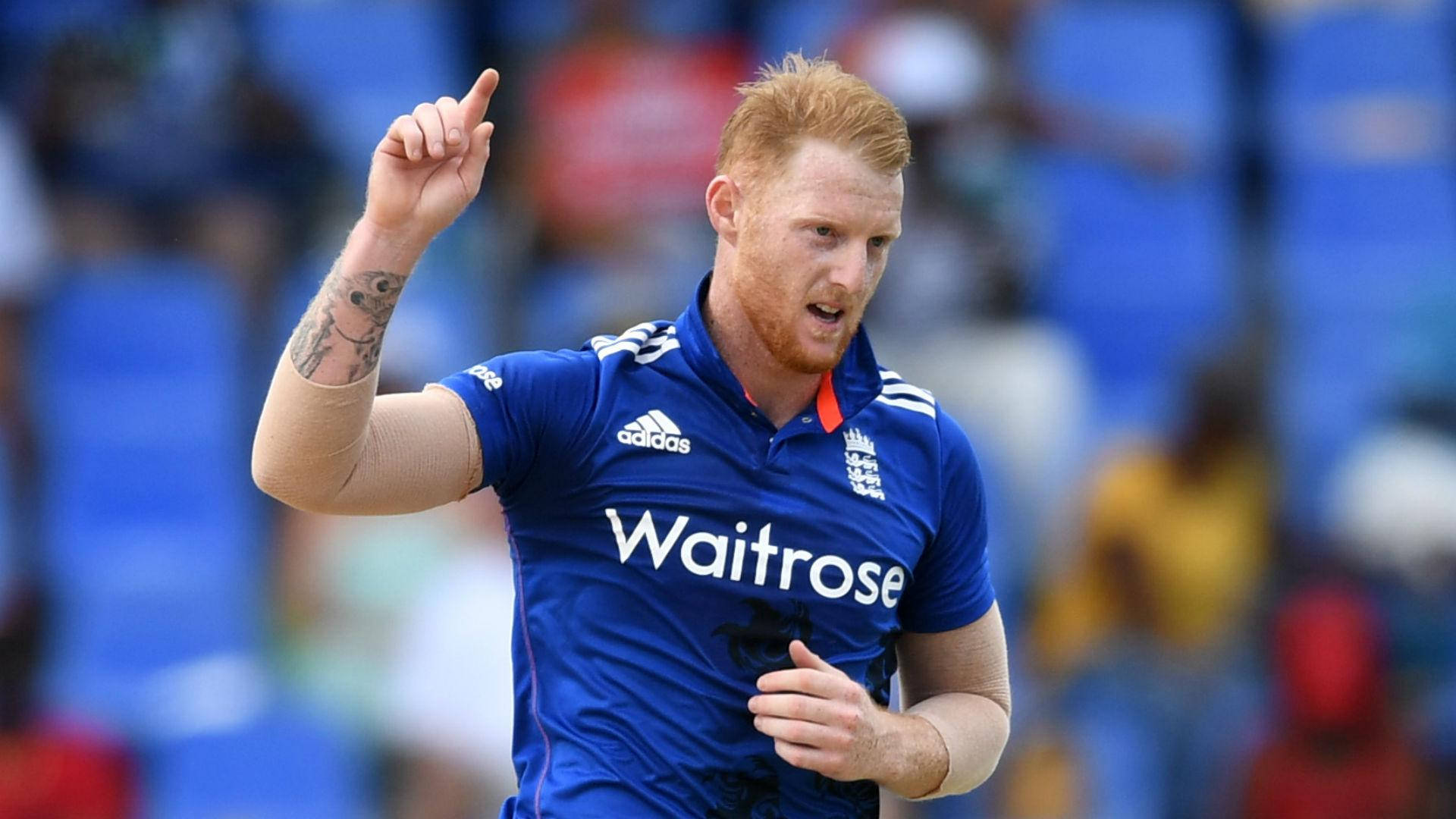 Ben Stokes 桌布 壁紙 — 一位紅髮板球運動員身穿藍色英格蘭球衣，在日間比賽中舉起手指慶祝。