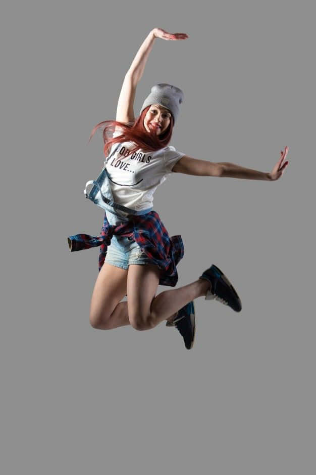 jump 桌布 壁紙 — 一位紅髮的快樂年輕女子在純灰色背景前以動態姿勢躍起。