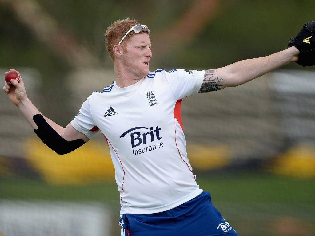 Ben Stokes 桌布 壁紙 — 一位紅髮的板球運動員身穿英格蘭隊服，在草地上準備投擲紅球。