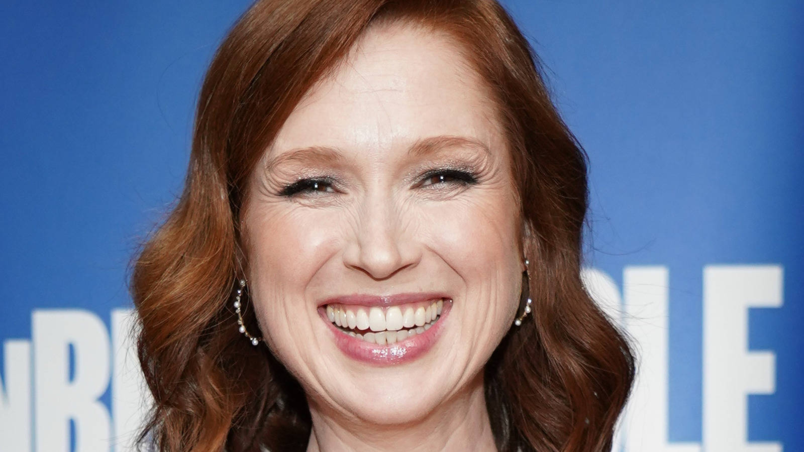unbreakable kimmy schmidt 桌布 壁紙 — 一位紅髮的耀眼女性在藍色背景上帶有白色字體前燦爛微笑。