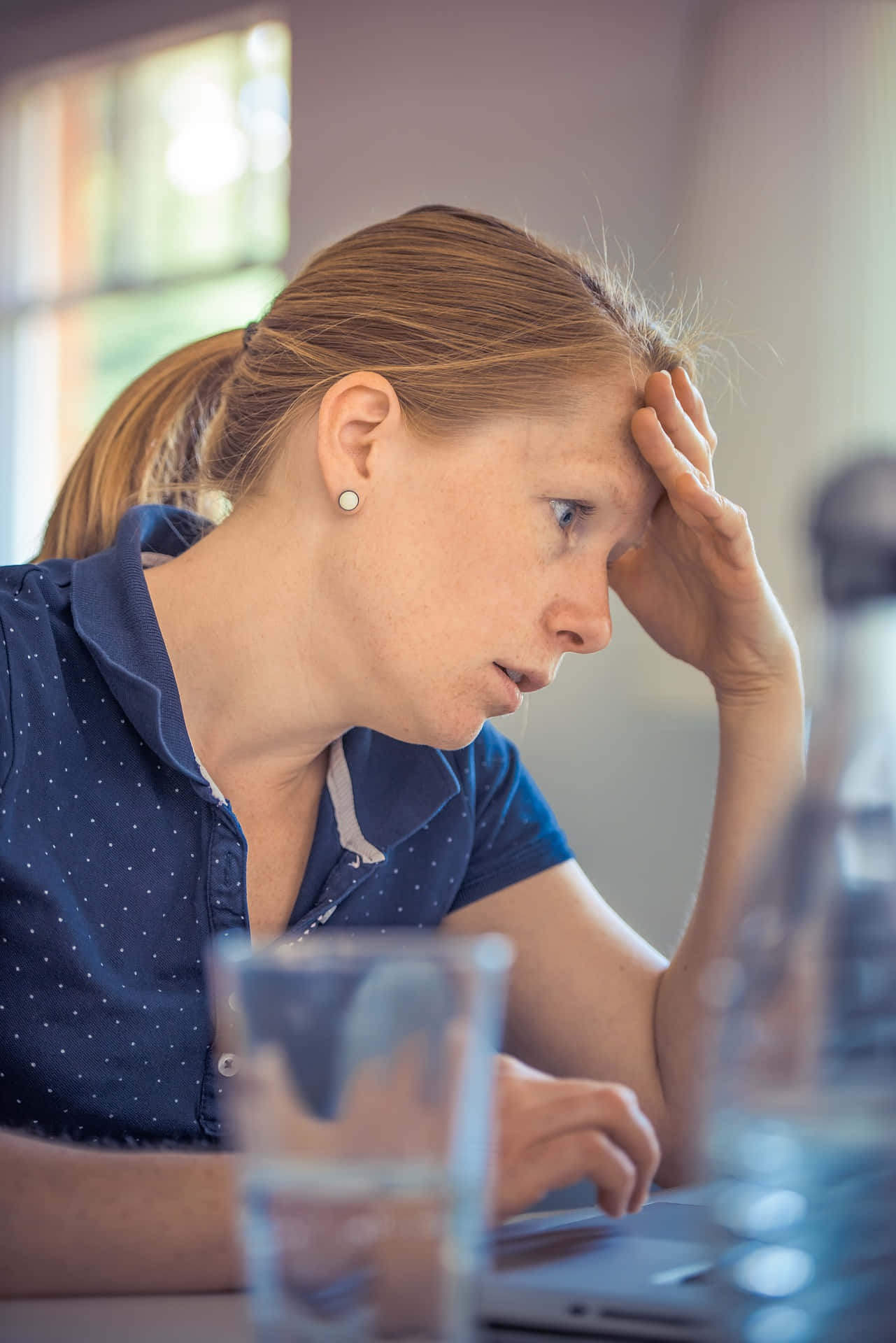 Frustrated 桌布 壁紙 — 一位紅髮紮成馬尾的女性，在柔和光線的房間裡，頭靠在手上看著筆記型電腦。