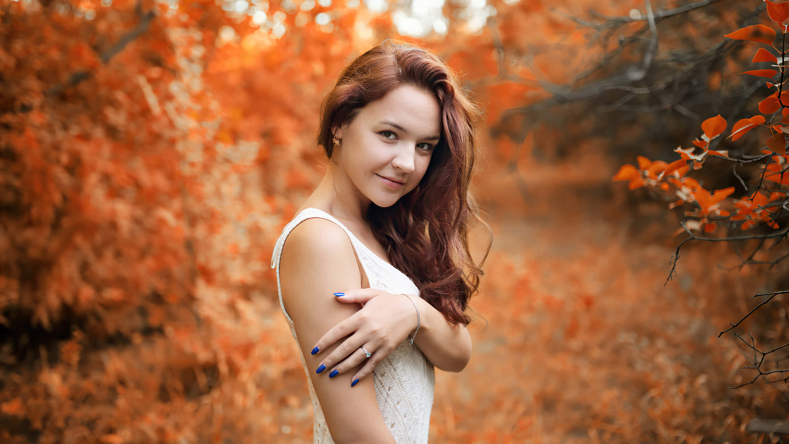 桌布 壁紙 — 一位紅髮藍指甲的女性在充滿鮮豔橙色秋葉的森林中溫柔微笑。