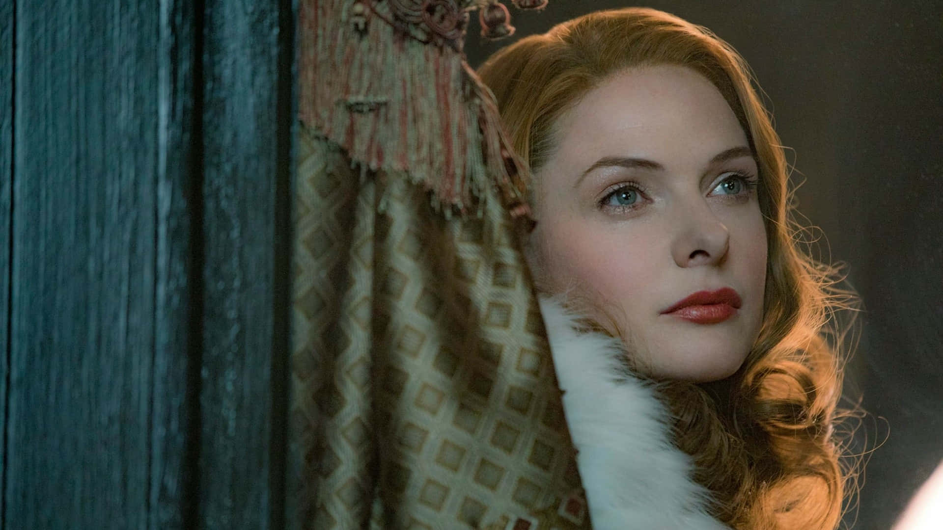 電影動圖 桌布 壁紙 — 一位紅髮藍眼的女性在昏暗的房間裡從華麗的窗簾後探出頭來。