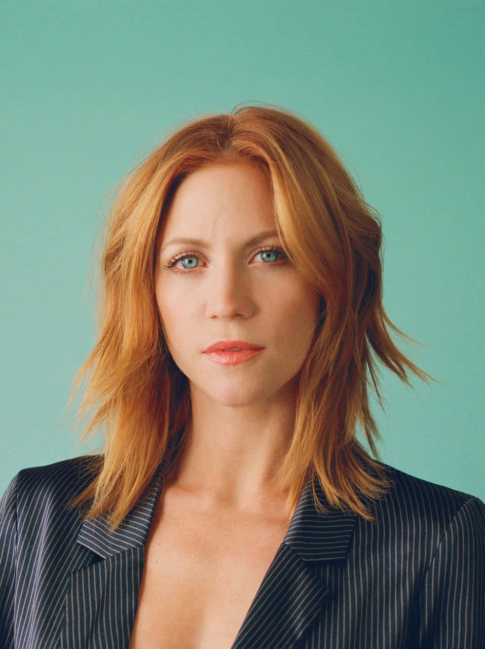 brittany snow 桌布 壁紙 — 一位紅髮藍眼的女性穿著細條紋西裝外套，背景為純青色。