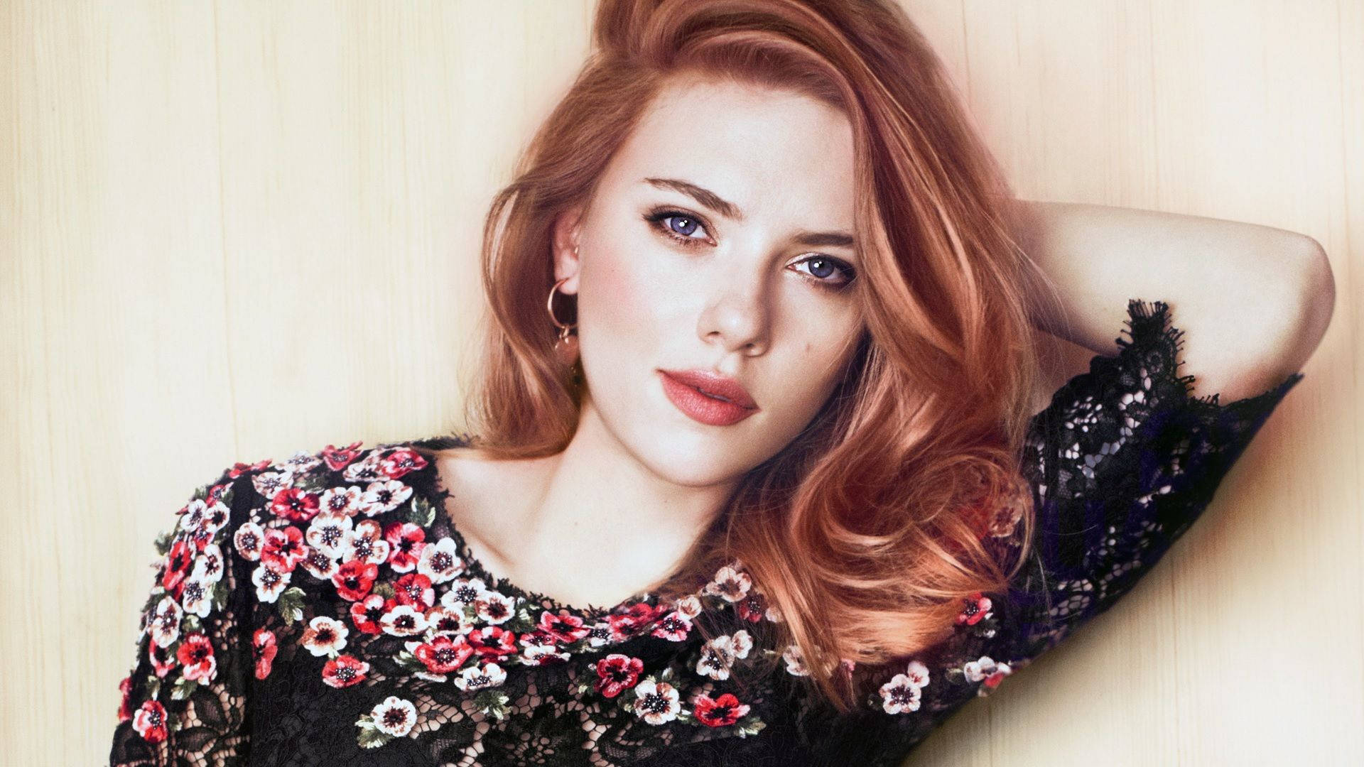 Scarlett 桌布 壁紙 — 一位紅髮藍眼的女性穿著黑色花卉蕾絲上衣，在淺色木質背景前直視鏡頭。