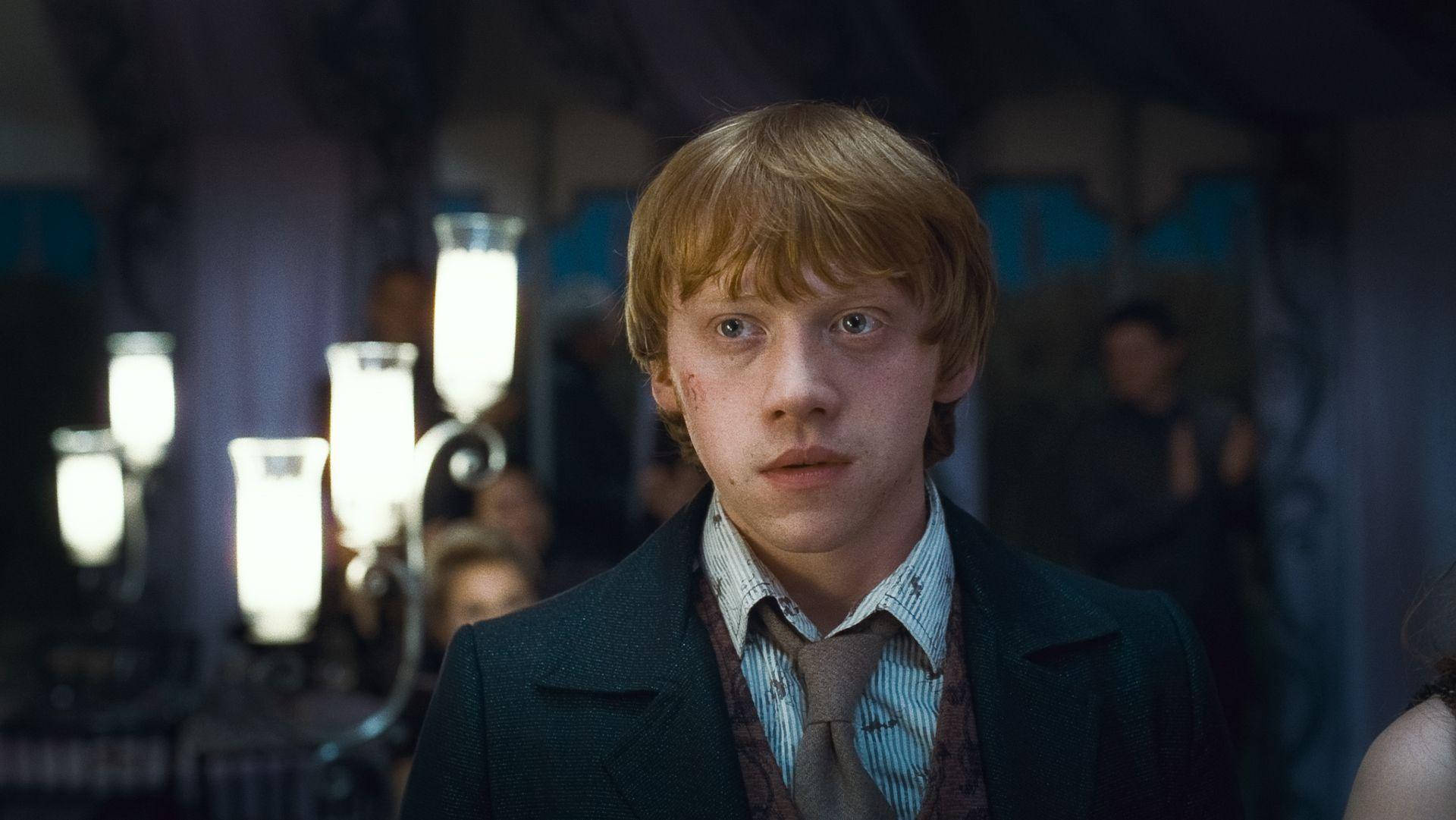 Ron Weasley 桌布 壁紙 — 一位紅髮雀斑的年輕男子在昏暗的房間裡凝視著，身後有發光的燭光。