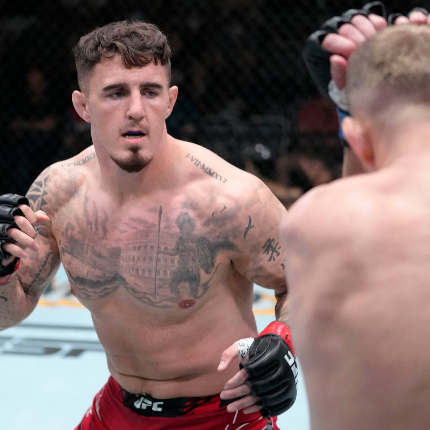 UFC 桌布 壁紙 — 一位紋身MMA拳手穿著紅色短褲，在UFC比賽中於籠內凝視對手。
