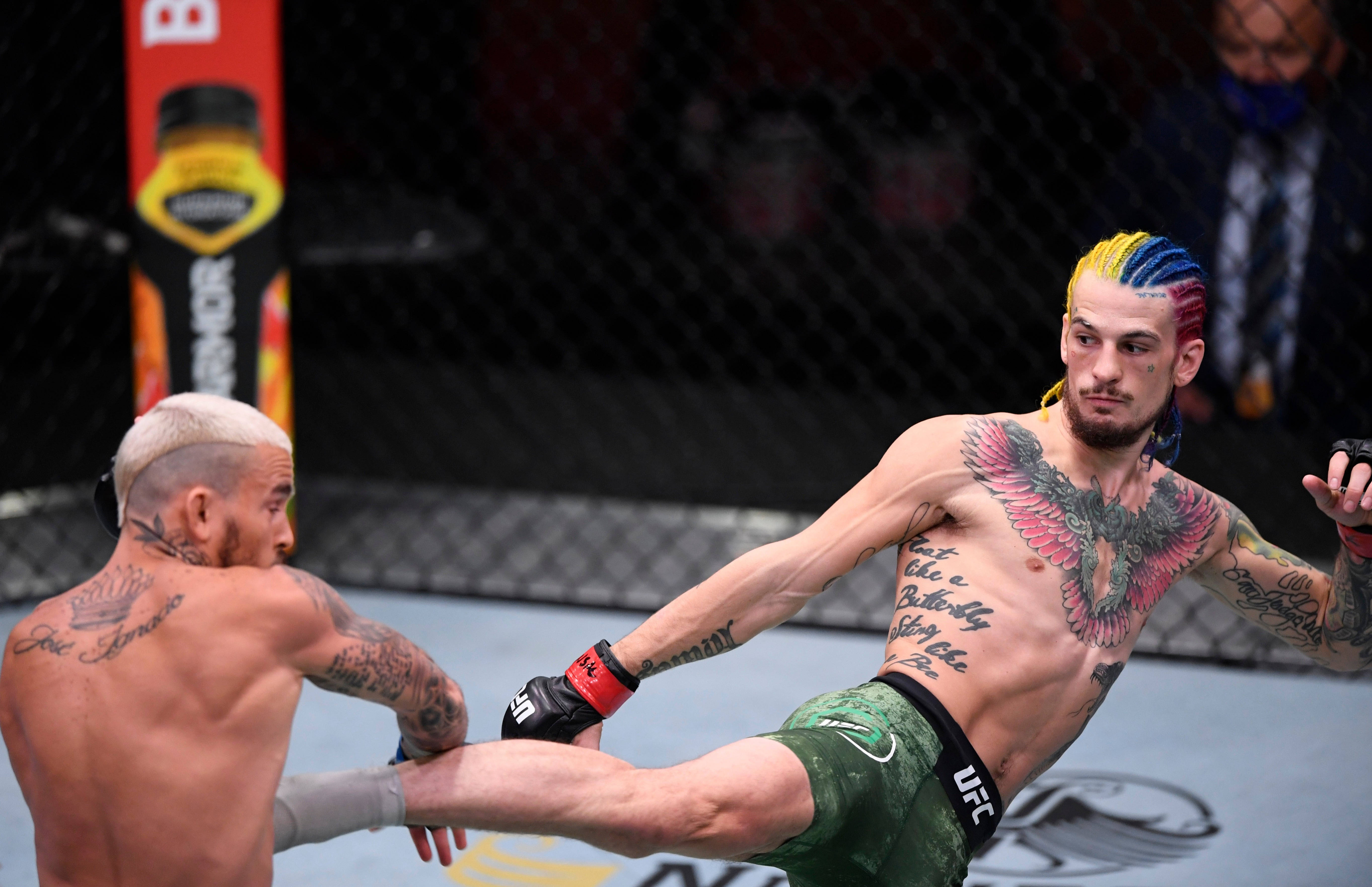 UFC 桌布 壁紙 — 一位紋身戰士擁有彩虹頭髮，在明亮的場館燈光下於UFC八角籠中向對手踢出高踢。
