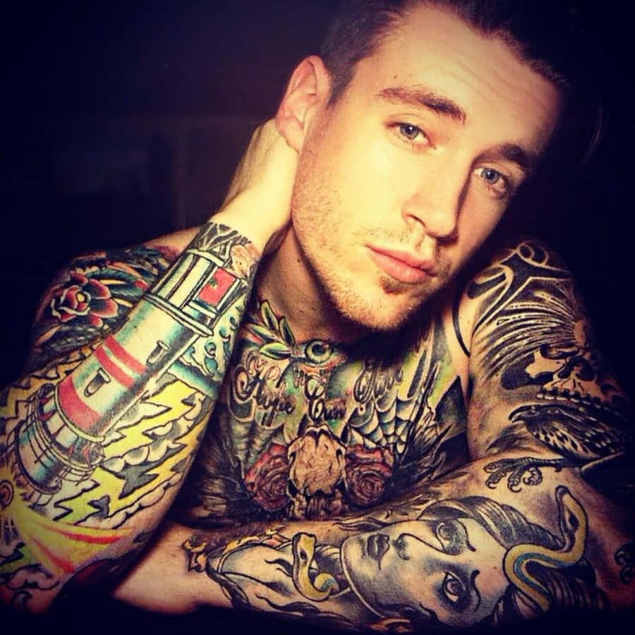 Tattoo Boy 桌布 壁紙 — 一位紋身男子，眼神銳利，手臂上有色彩繽紛的紋身，在深色背景前擺姿勢。