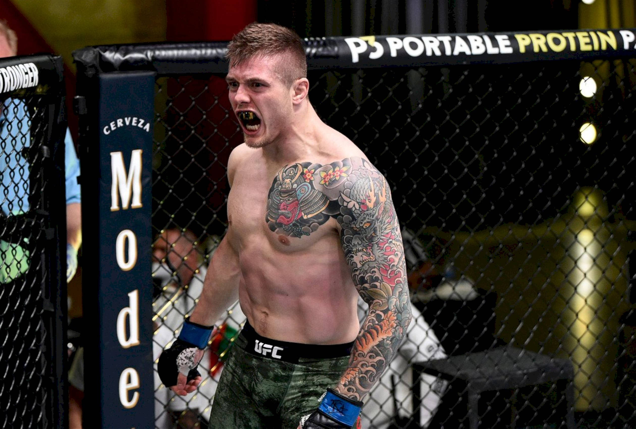 UFC 桌布 壁紙 — 一位紋身的MMA拳手在明亮的場館燈光下，在UFC八角籠內憤怒咆哮。