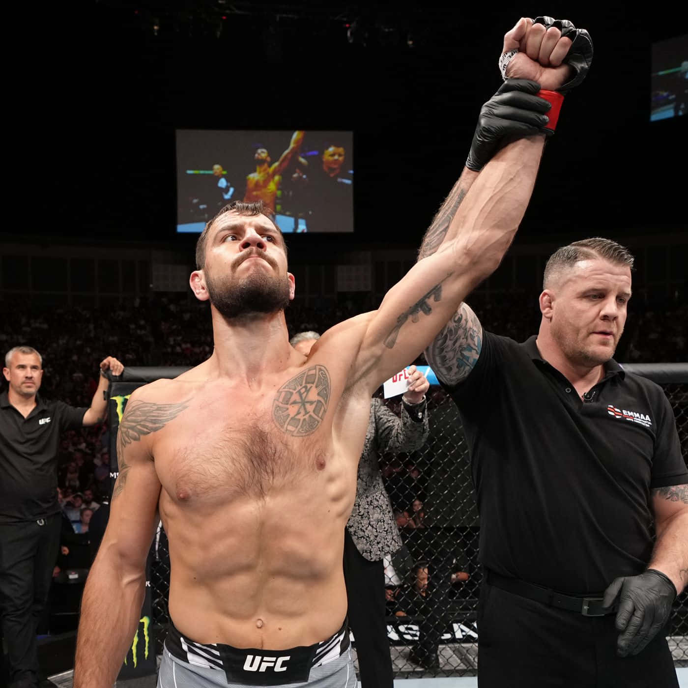 桌布 壁紙 — 一位紋身的UFC勝利拳手在八角籠中舉起戴手套的拳頭，裁判高舉他的手臂。