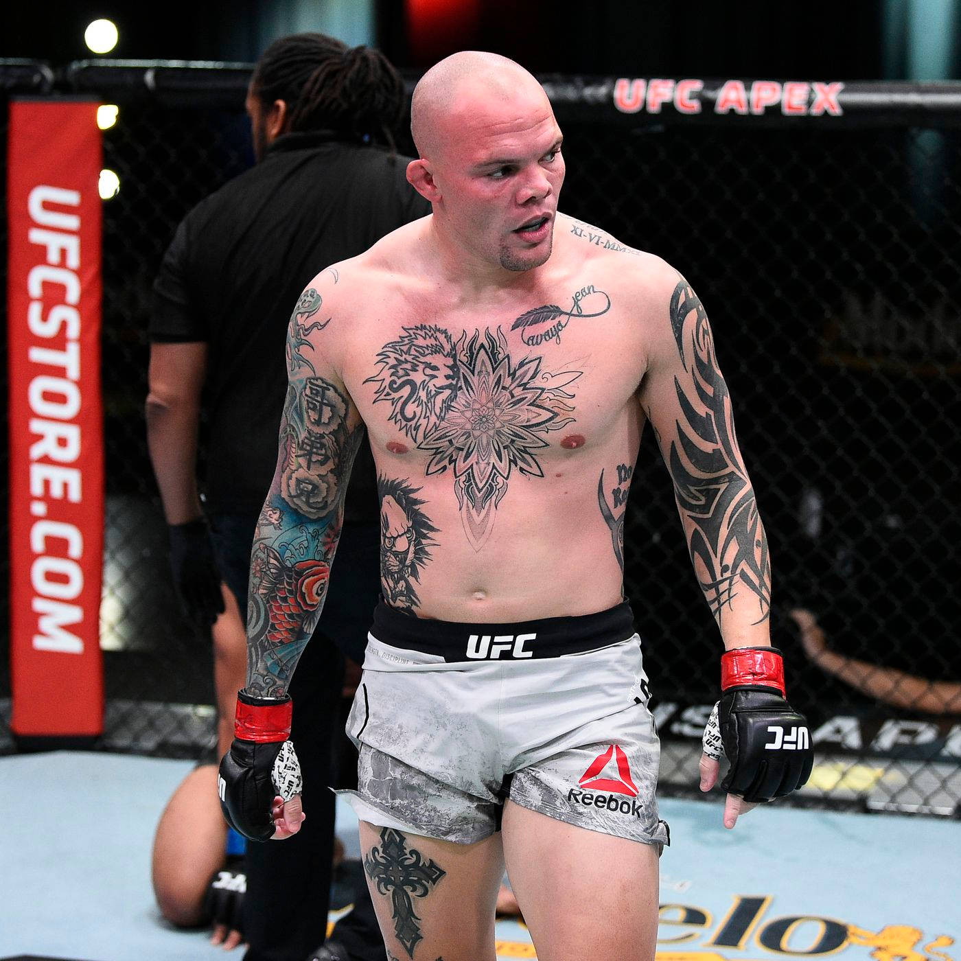 MMA 桌布 壁紙 — 一位紋身的UFC拳手戴著手套和短褲，帶著強烈的專注力站在八角籠內。