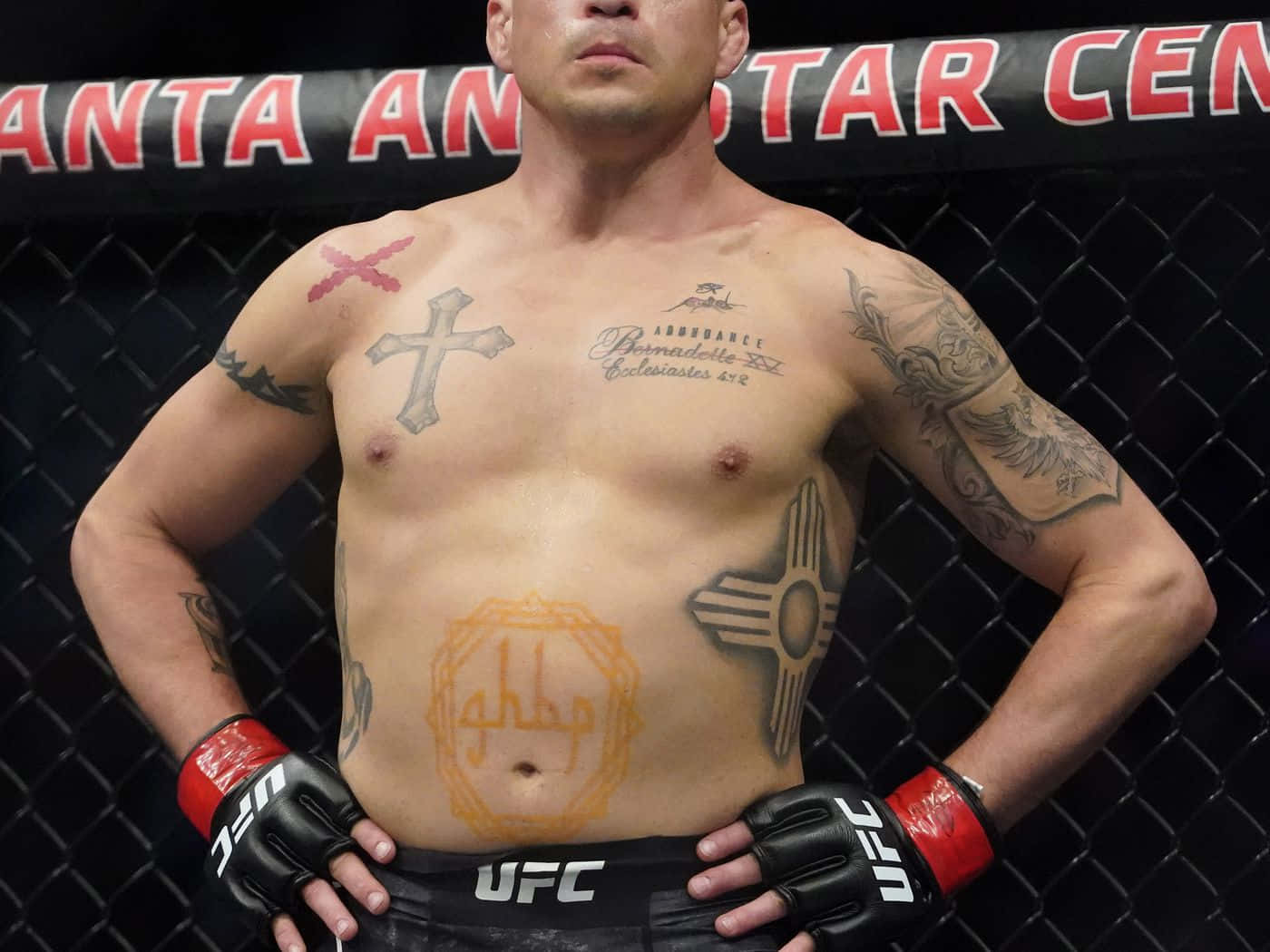 MMA 桌布 壁紙 — 一位紋身的UFC拳手自信地站在八角籠中，雙手叉腰，戴著手套和短褲。