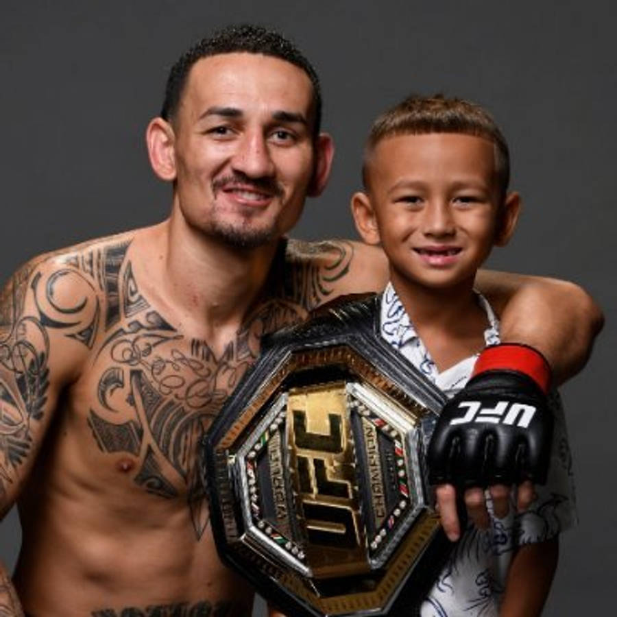 UFC 桌布 壁紙 — 一位紋身的UFC拳手自豪地微笑，與他年幼的兒子一起在深色工作室背景中拿著冠軍腰帶。