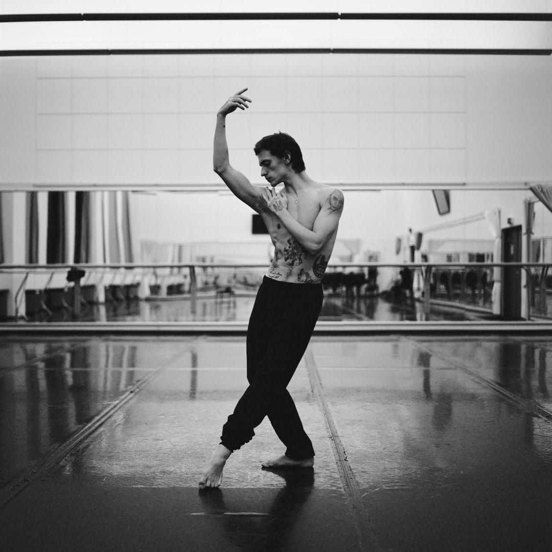 dancer 桌布 壁紙 — 一位紋身舞者在工作室中舉起一隻手臂，擺出優雅的姿勢，在單色燈光下反射在鏡牆上。
