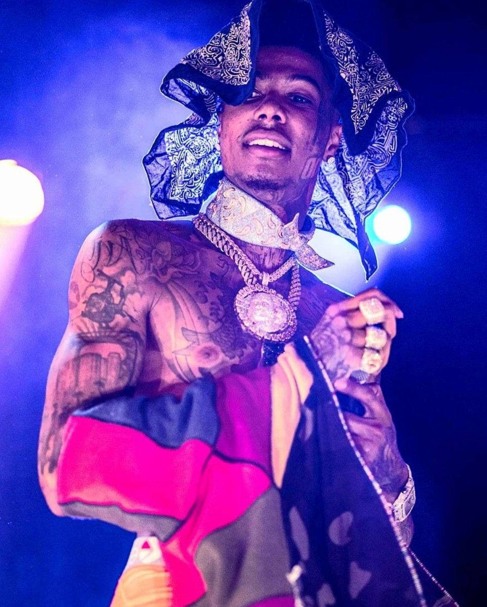 Celebrity 桌布 壁紙 — 一位紋身表演者戴著圖案帽子和金鏈，在藍色舞台燈光下微笑著拿著麥克風。