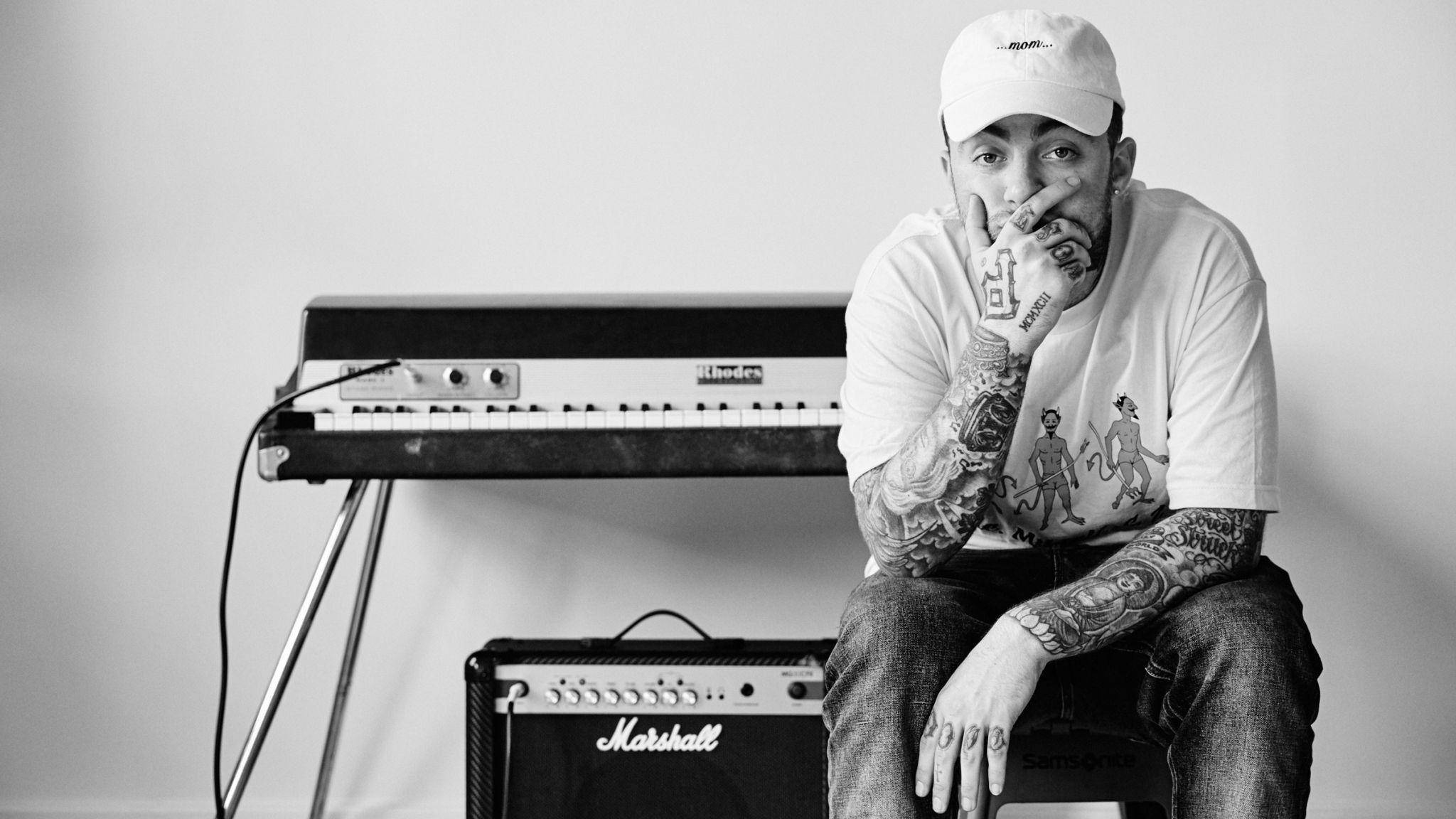 Mac Miller 桌布 壁紙 — 一位紋身音樂家戴著白色帽子，在簡約的工作室裡沉思地坐在鍵盤和Marshall擴音器旁邊。