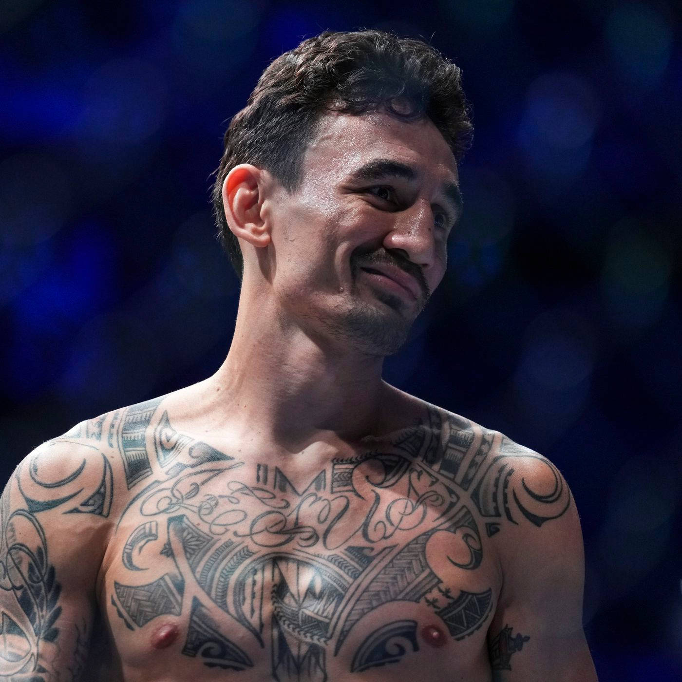 UFC 桌布 壁紙 — 一位紋身鬥士在模糊的藍色背景的競技場燈光下自信地微笑。