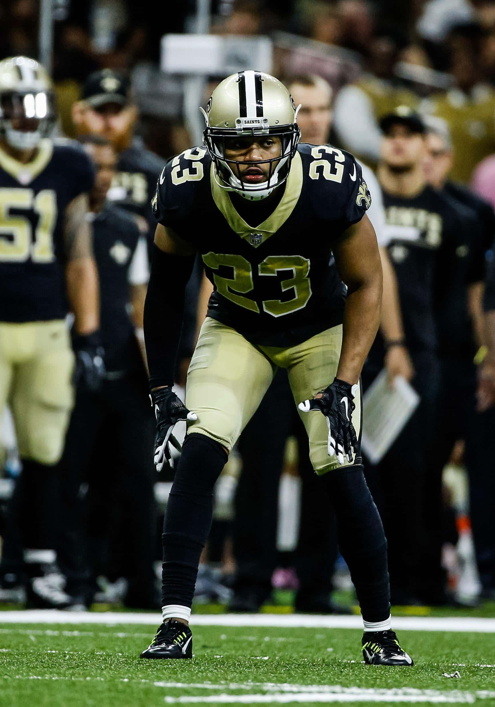 New Orleans Saints 桌布 壁紙 — 一位紐奧良聖徒隊的美式足球員身穿黑色和金色球衣，在球場燈光下於比賽中激烈地蹲伏在場上。