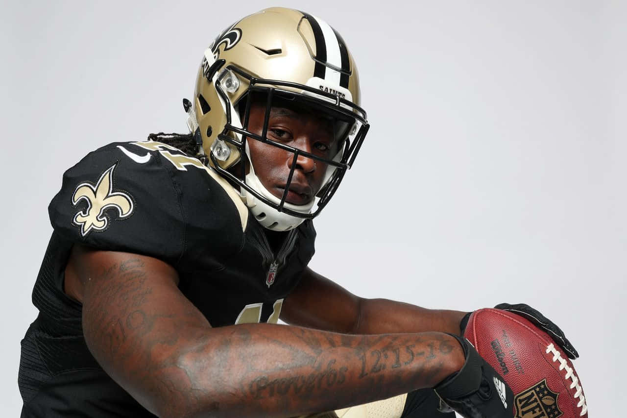 Alvin Kamara 桌布 壁紙 — 一位紐奧良聖徒隊的美式足球員身穿黑色和金色裝備，在純白色背景前專注地緊握著足球。