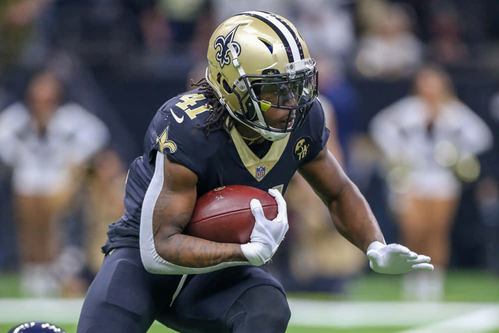 Fantasy Football Profile 桌布 壁紙 — 一位紐奧良聖徒隊的美式足球員身穿海軍藍和金色裝備，在球場燈光下於比賽中持球衝刺。