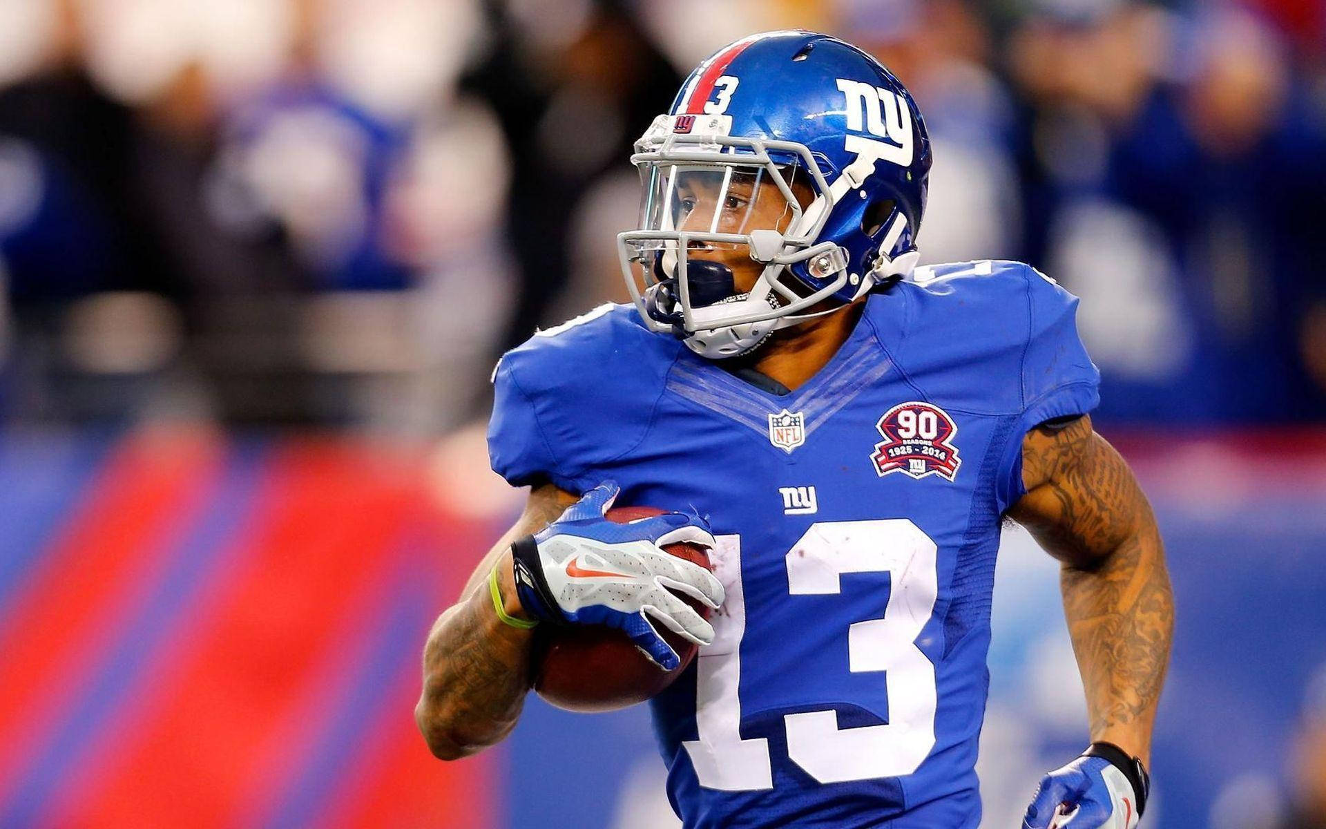 Odell 桌布 壁紙 — 一位紐約巨人隊美式足球員身穿藍色球衣13號，在球場燈光下帶球奔跑。