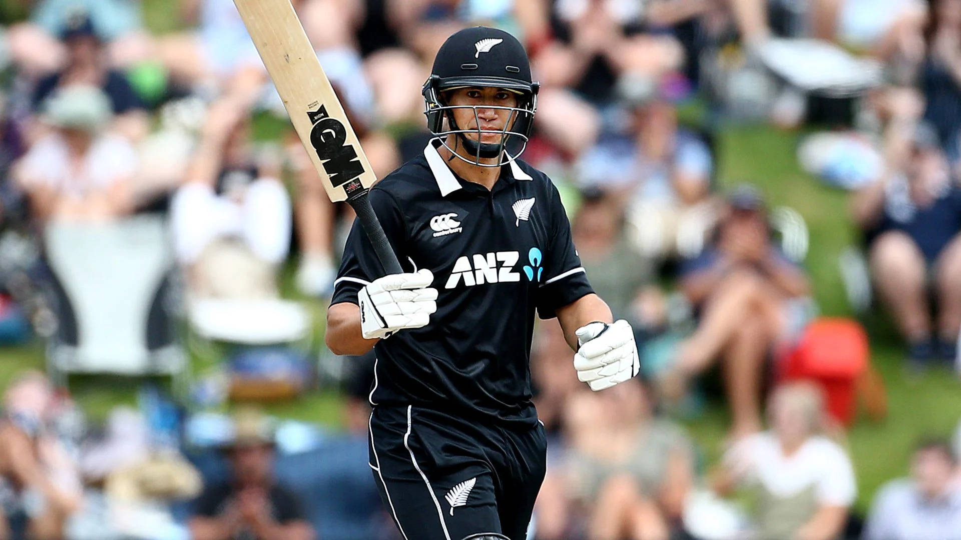 Ross Taylor 桌布 壁紙 — 一位紐西蘭板球球員身穿黑色制服和頭盔，高舉球棒慶祝勝利，背景有觀眾歡呼。