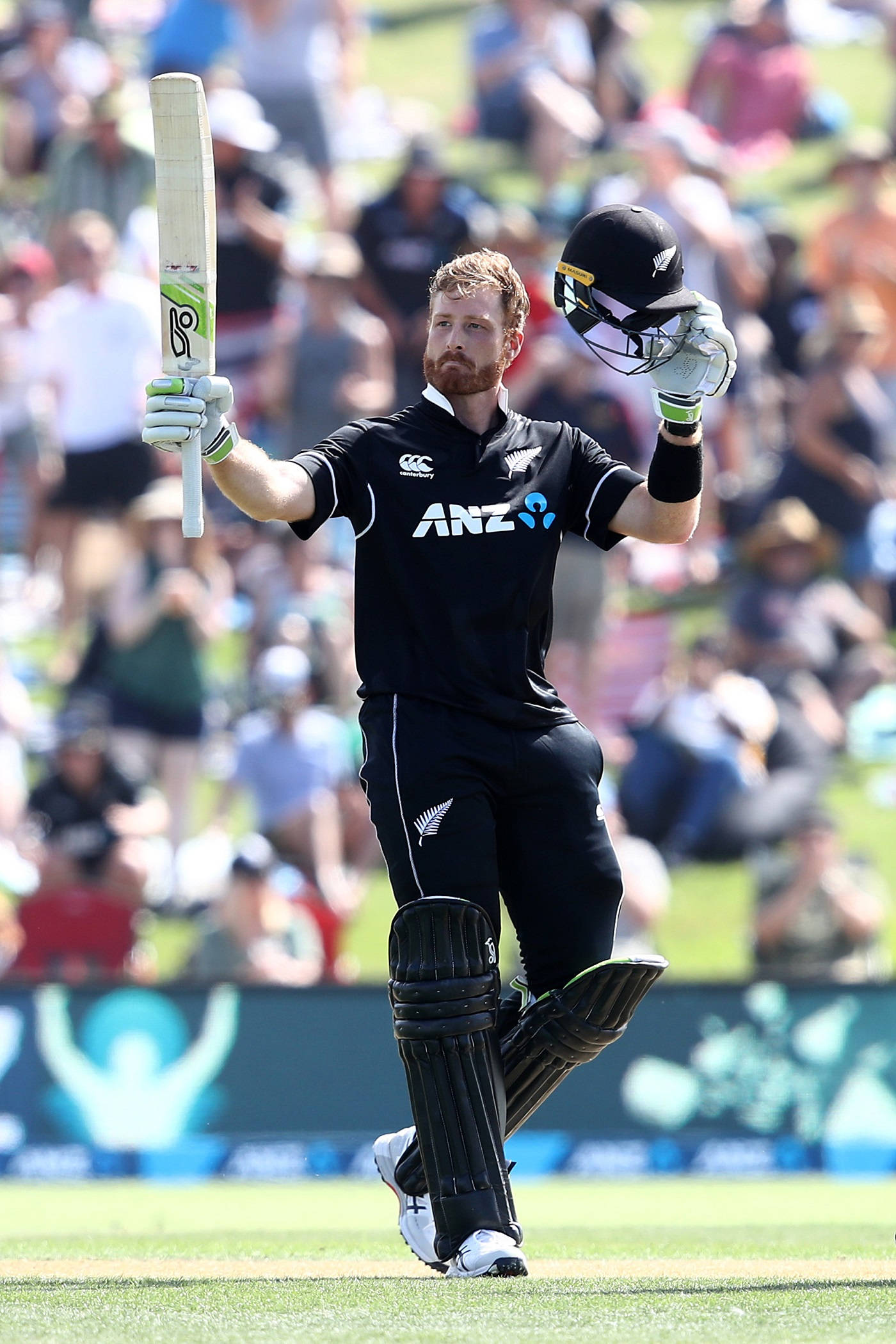 martin guptill 桌布 壁紙 — 一位紐西蘭板球運動員在陽光明媚的日子裡，在歡呼的球迷面前高舉球棒和頭盔慶祝。