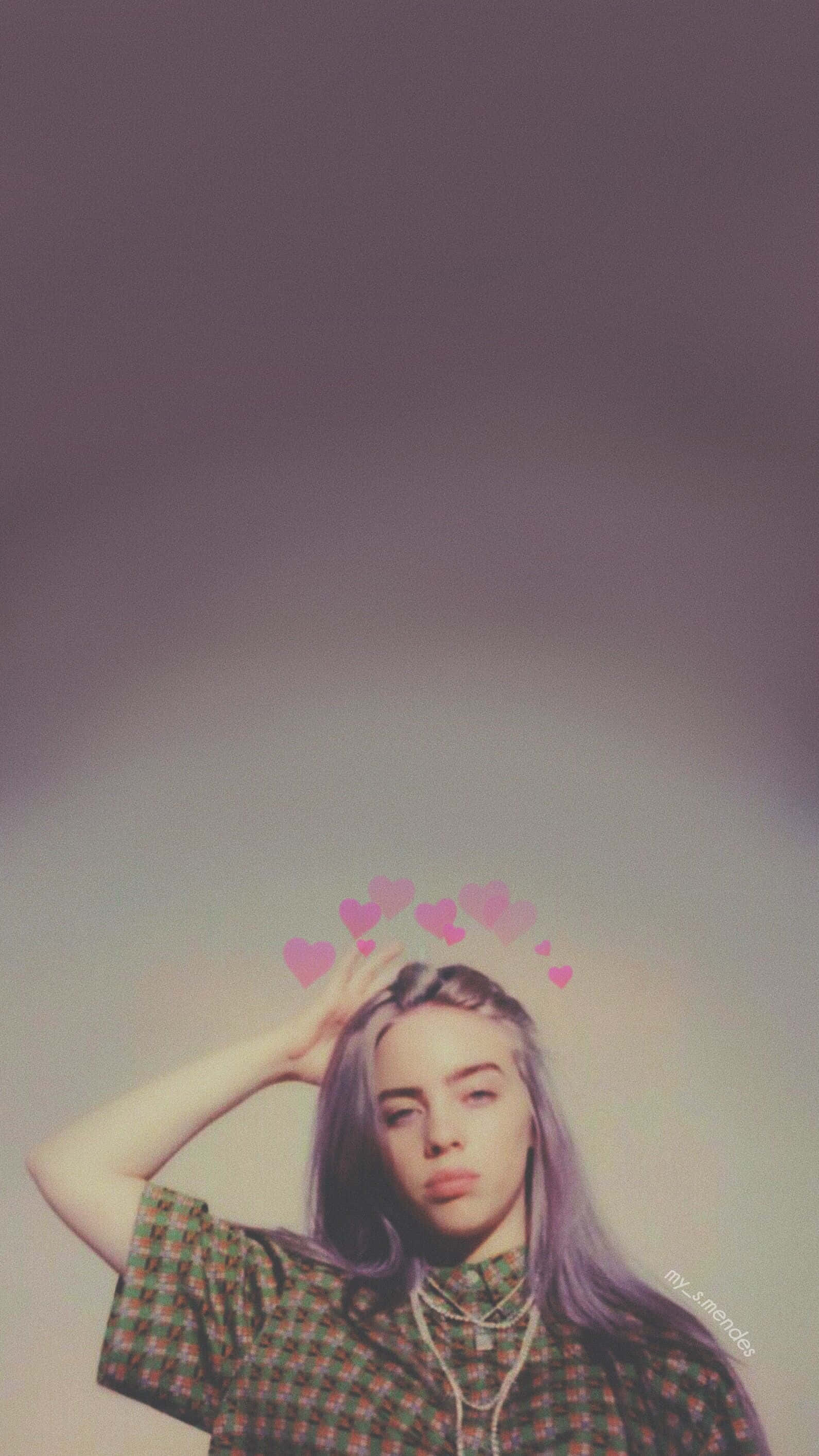 Billie Eilish Purple 桌布 壁紙 — 一位紫髮年輕女性在柔和漸變背景前擺姿勢，粉紅色心形漂浮在她頭頂上方。