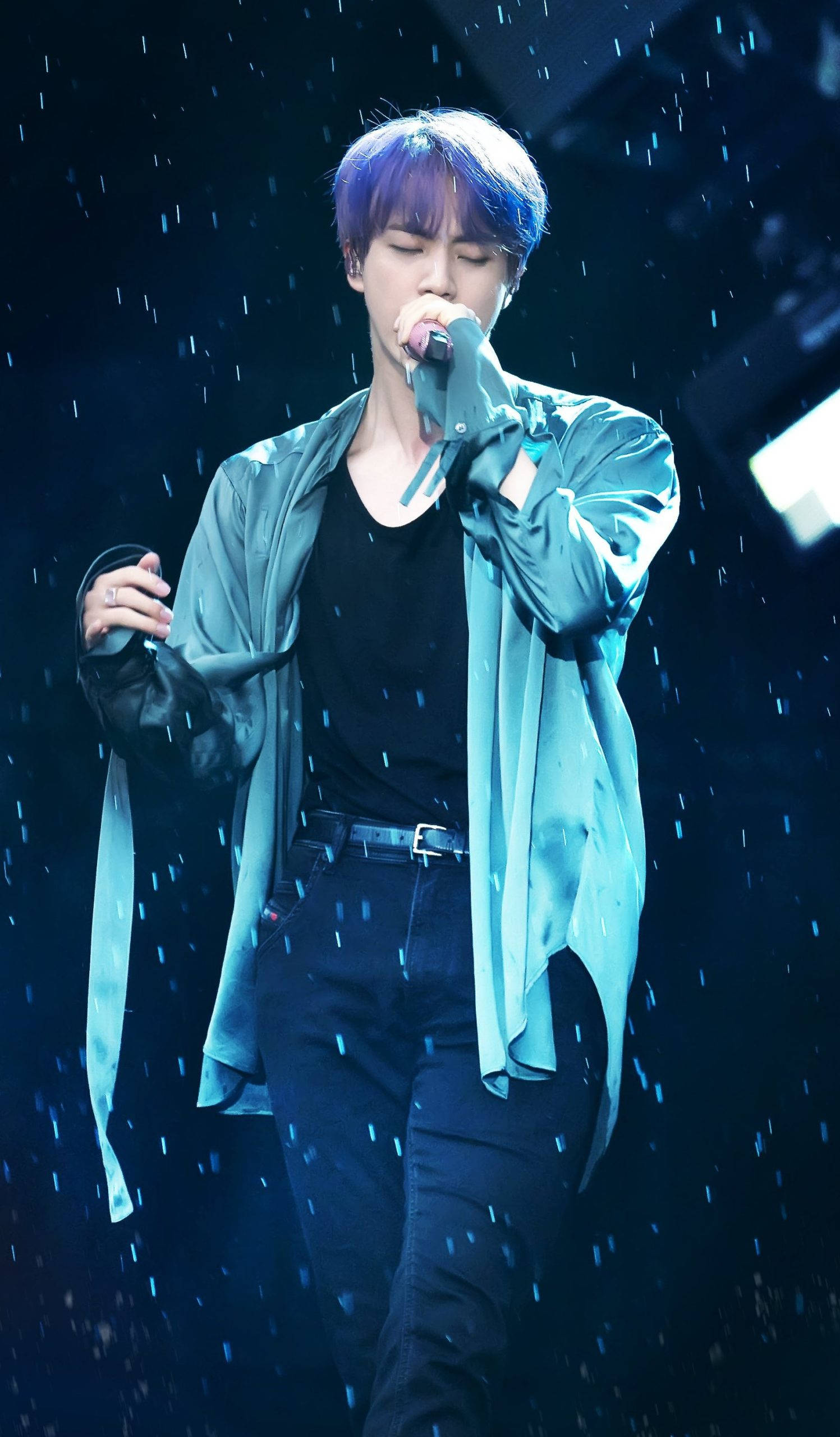 kim seok jin 桌布 壁紙 — 一位紫髮男歌手在藍色舞台燈光下對著麥克風熱情演唱，周圍有模擬雨水落下。