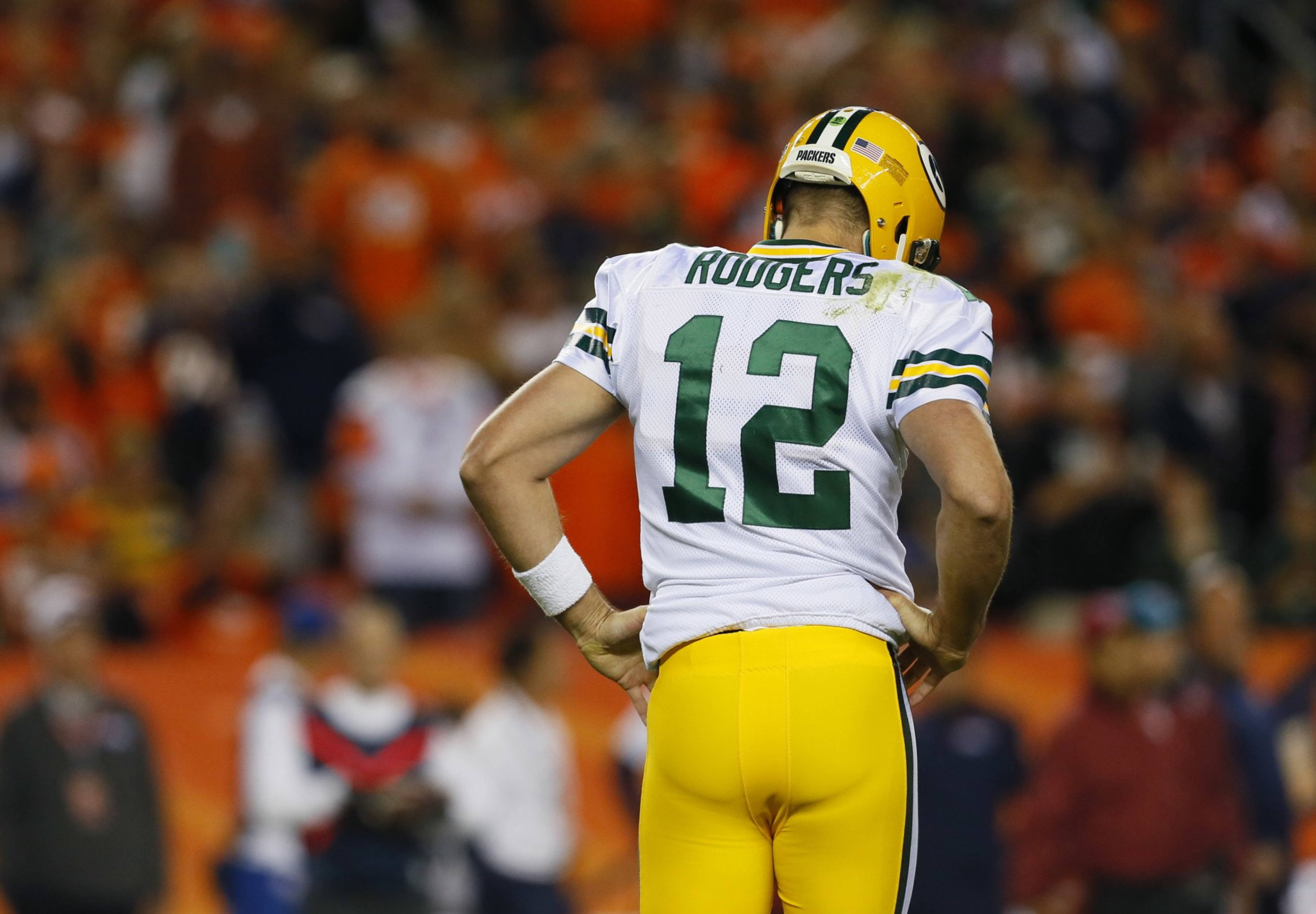 Aaron Rodgers 桌布 壁紙 — 一位綠灣包裝工的四分衛身穿白色12號球衣，雙手叉腰，面向一群模糊的橙色衣著球迷。