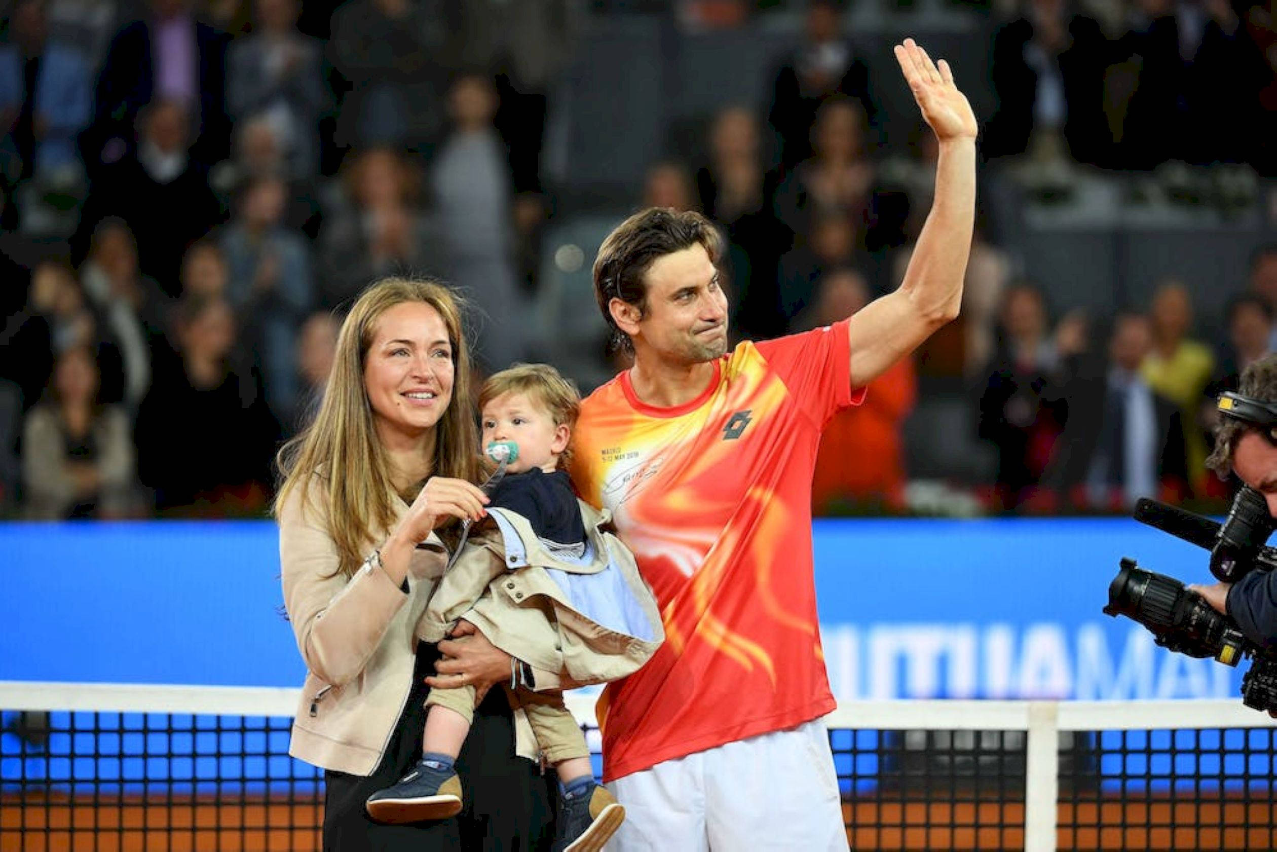 Tennis 桌布 壁紙 — 一位網球運動員在夜間球場上抱著孩子，妻子站在他們旁邊，向球迷揮手。