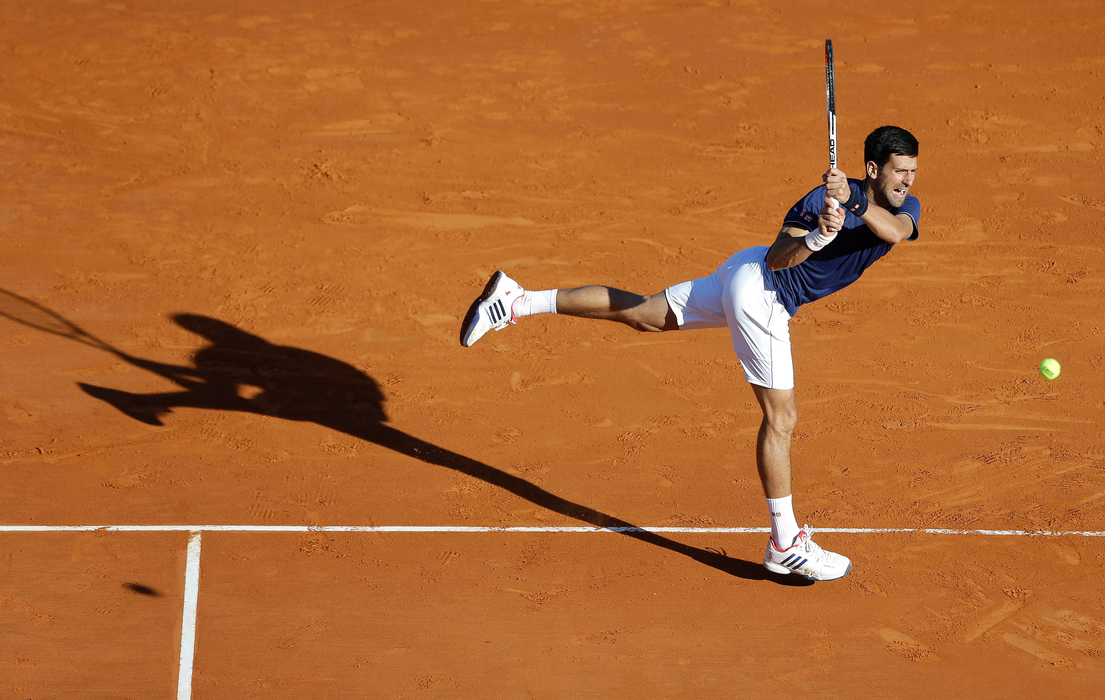 Novak 桌布 壁紙 — 一位網球運動員在陽光明媚的紅土球場上動態跳躍，以高度專注和運動優雅擊球。