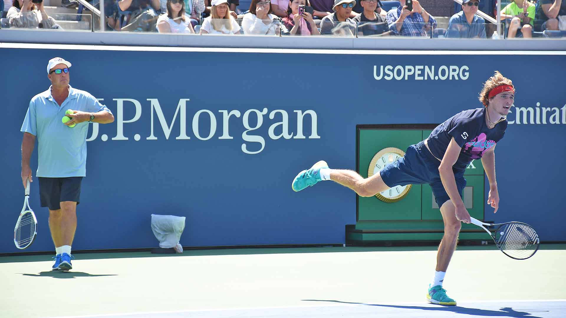 Tennis 桌布 壁紙 — 一位網球運動員在陽光明媚的美國公開賽中跳起擊出正手，附近有一名球童。