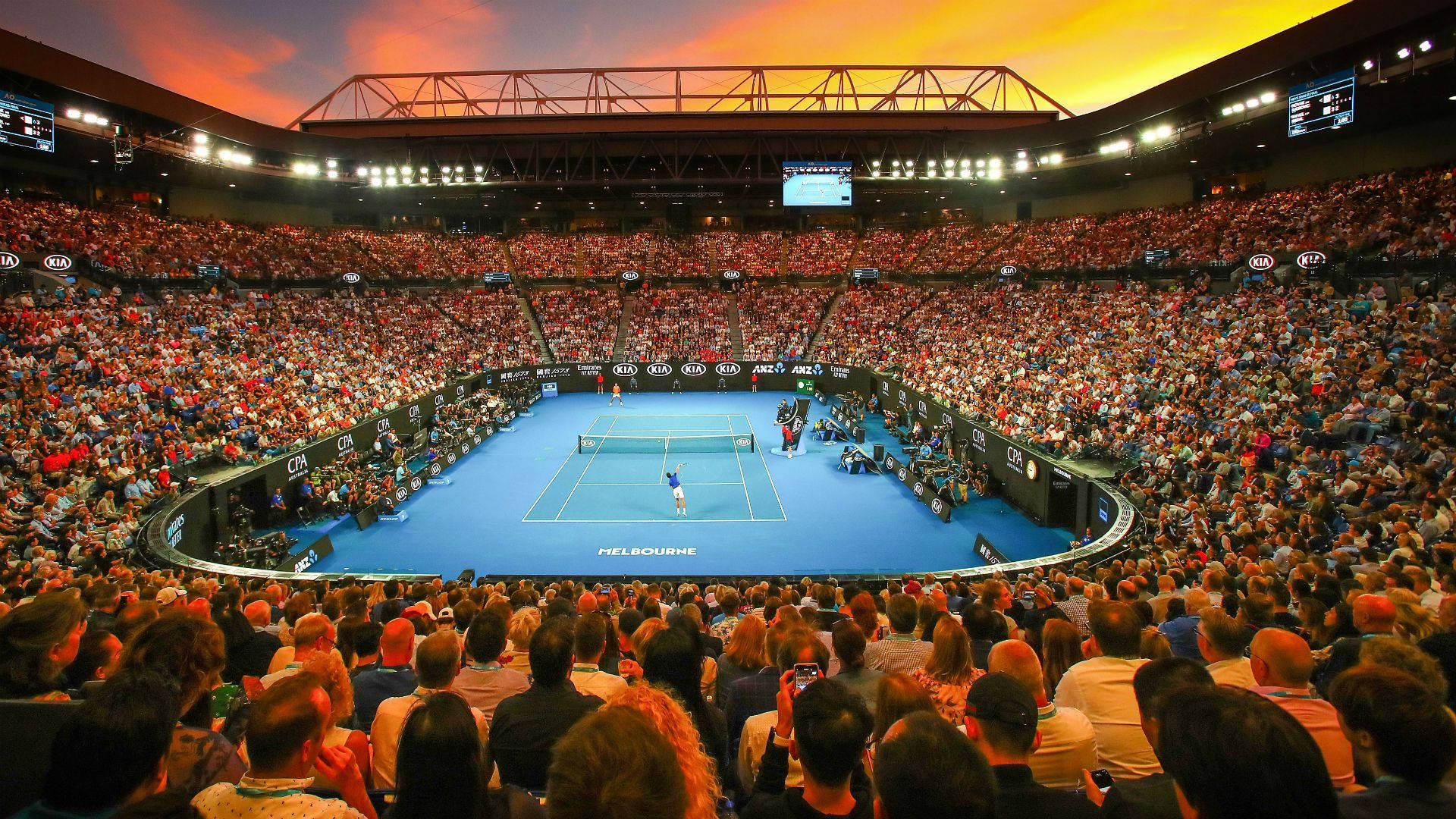 Australian Open 桌布 壁紙 — 一位網球選手在火紅的日落天空下，在擠滿觀眾的體育館中進行大滿貫比賽時發球。