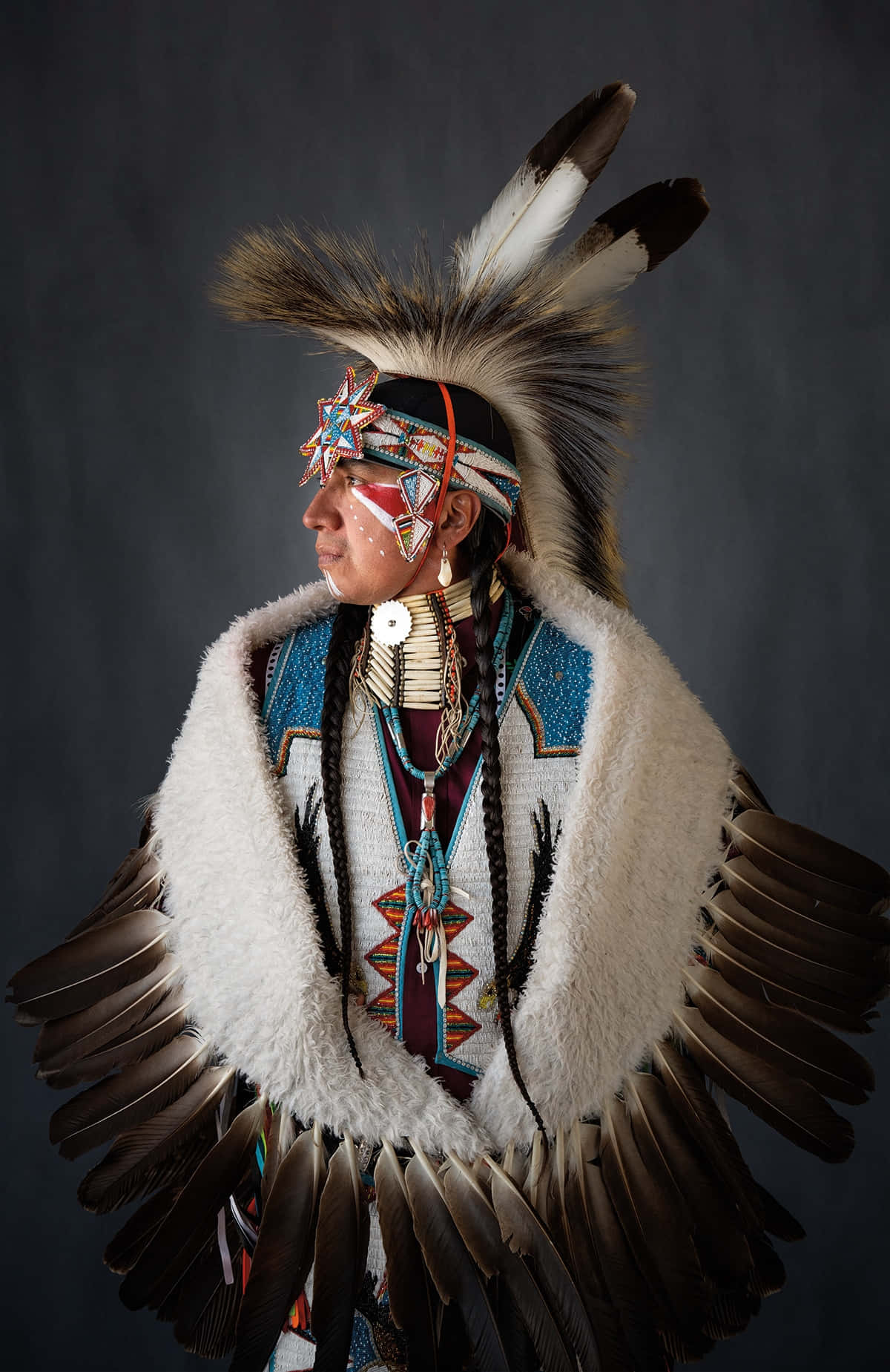 Native American 桌布 壁紙 — 一位美洲原住民男子穿著傳統服飾，頭戴羽毛頭飾，身著珠飾服裝，在黑暗的攝影棚背景下擺姿勢。