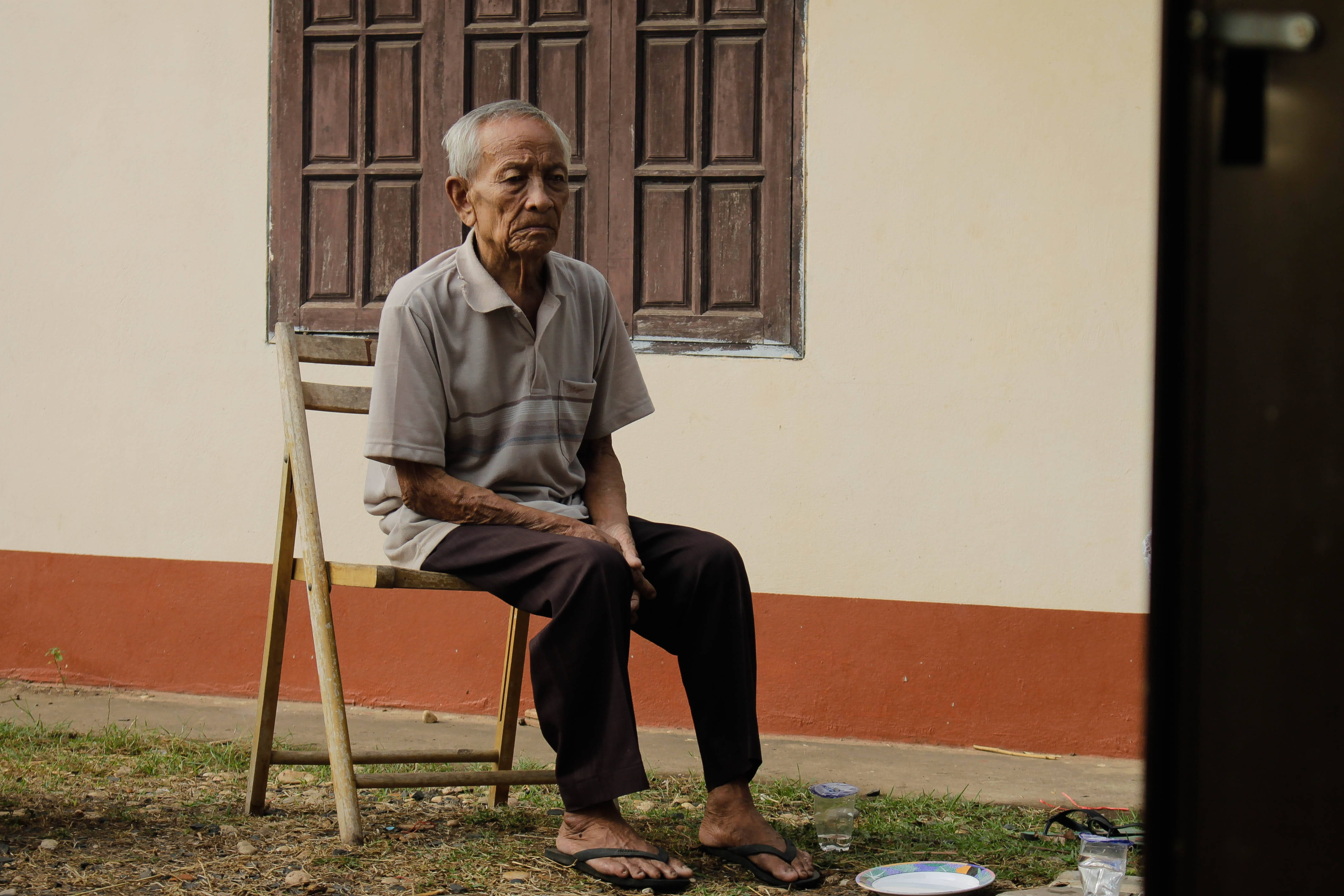 Man 桌布 壁紙 — 一位老人靜靜地坐在一棟建築物外的木椅上，建築物有風化的百葉窗和紅色條紋。