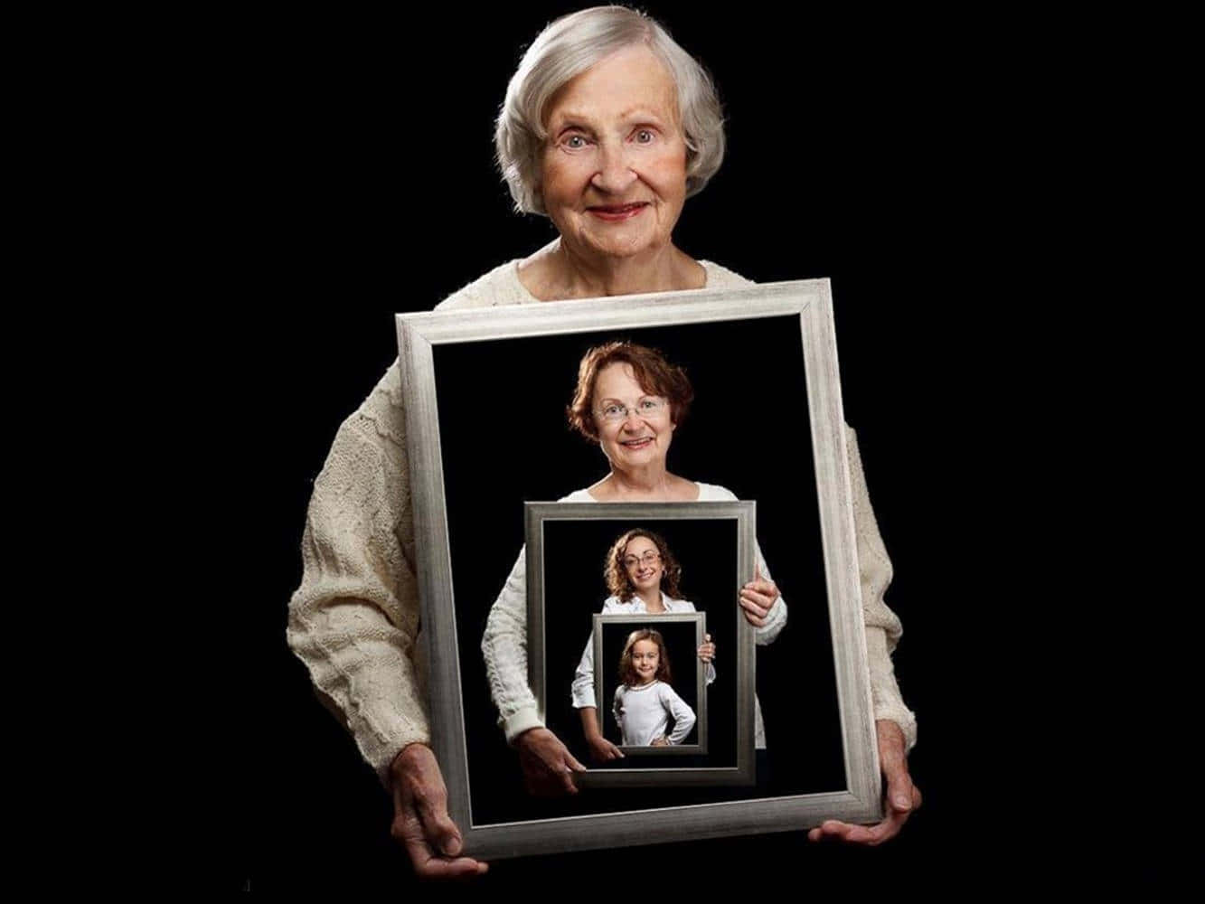 Old Lady 桌布 壁紙 — 一位老婦人微笑著手持一個相框，裡面是她年輕時的照片，而照片中的她手持一個更小的相框，裡面是更年輕的自己，在黑色背景上形成一個遞迴肖像。