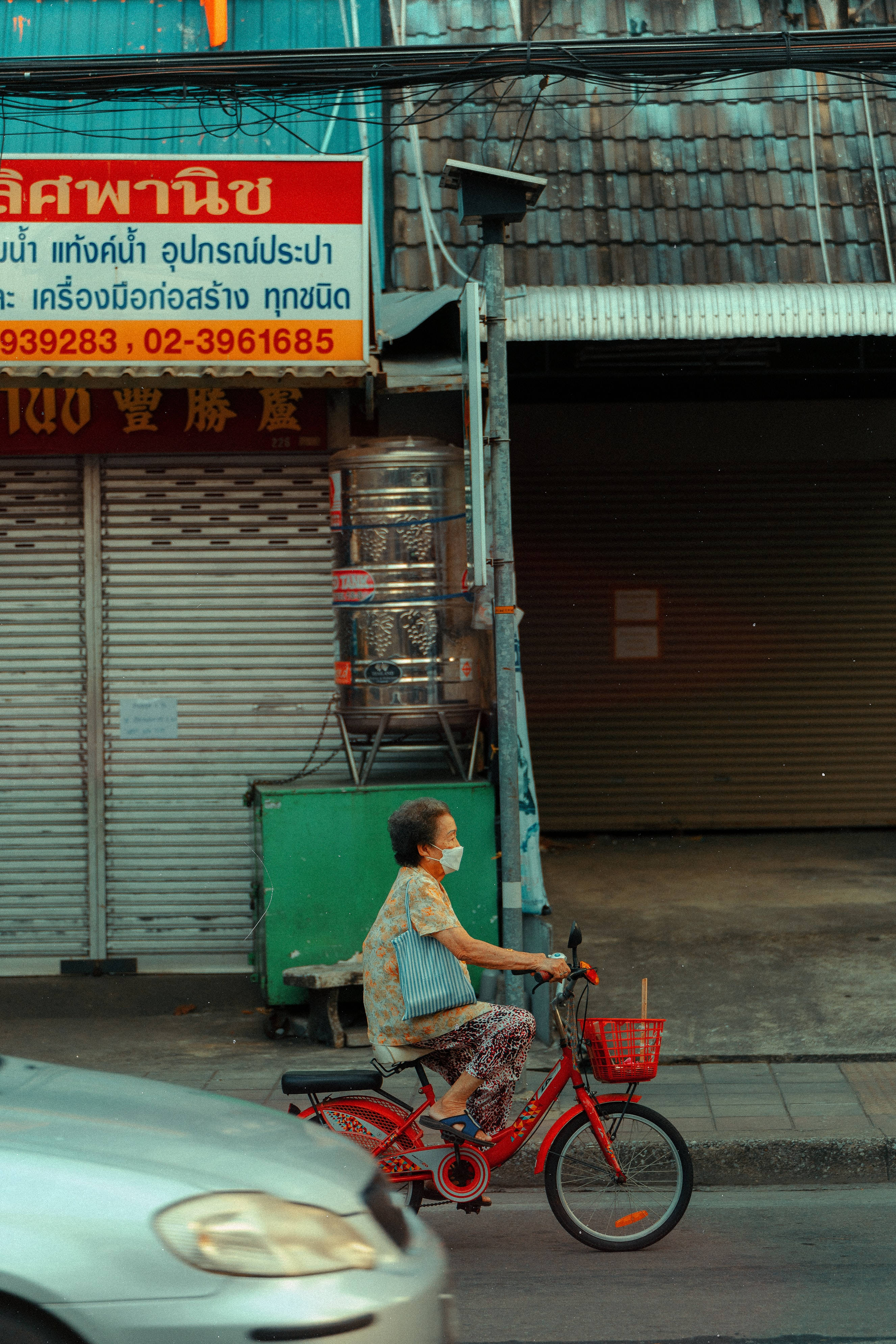 Street 桌布 壁紙 — 一位老婦人騎著紅色腳踏車，經過已關門的商店和纏繞的電線，在繁忙的城市小巷中。