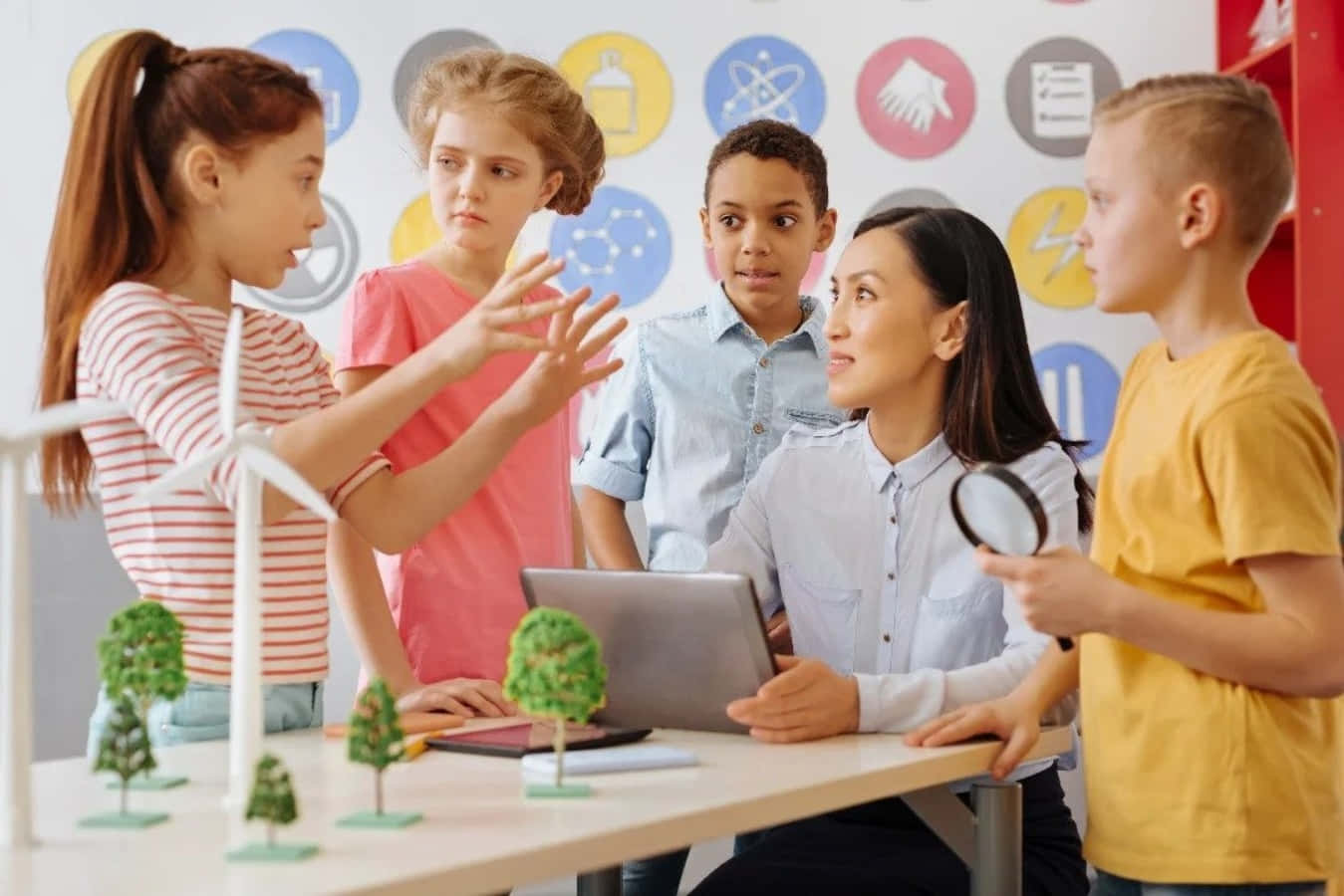 Learning 桌布 壁紙 — 一位老師和四個不同背景的孩子圍著一張桌子，桌上放有風力渦輪機模型和一部筆記型電腦，專注於科學課堂。