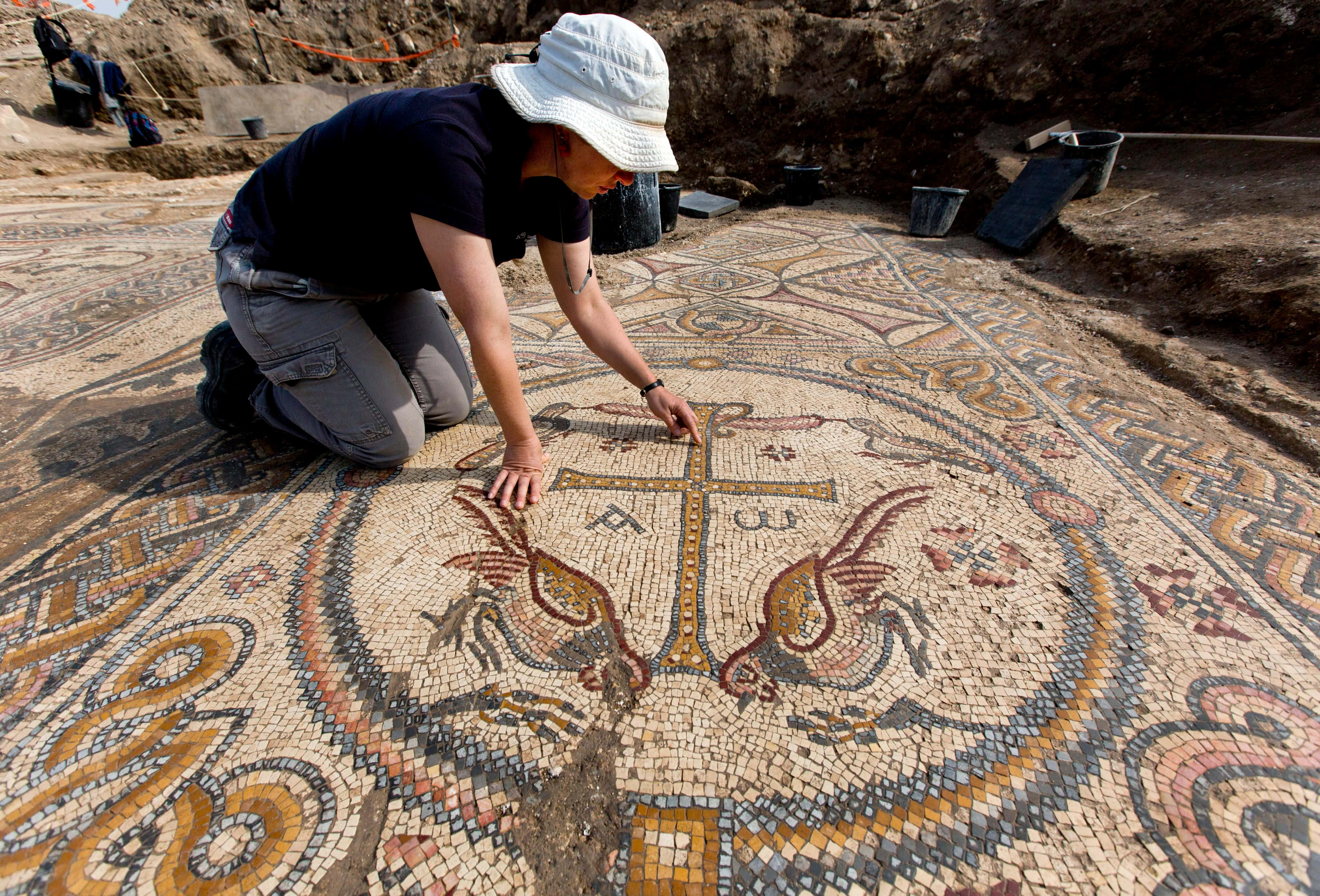 Mosaic 桌布 壁紙 — 一位考古學家跪在一個古老的馬賽克地板上，地板上有鳥類和十字架圖案，周圍是挖掘工具和泥土。