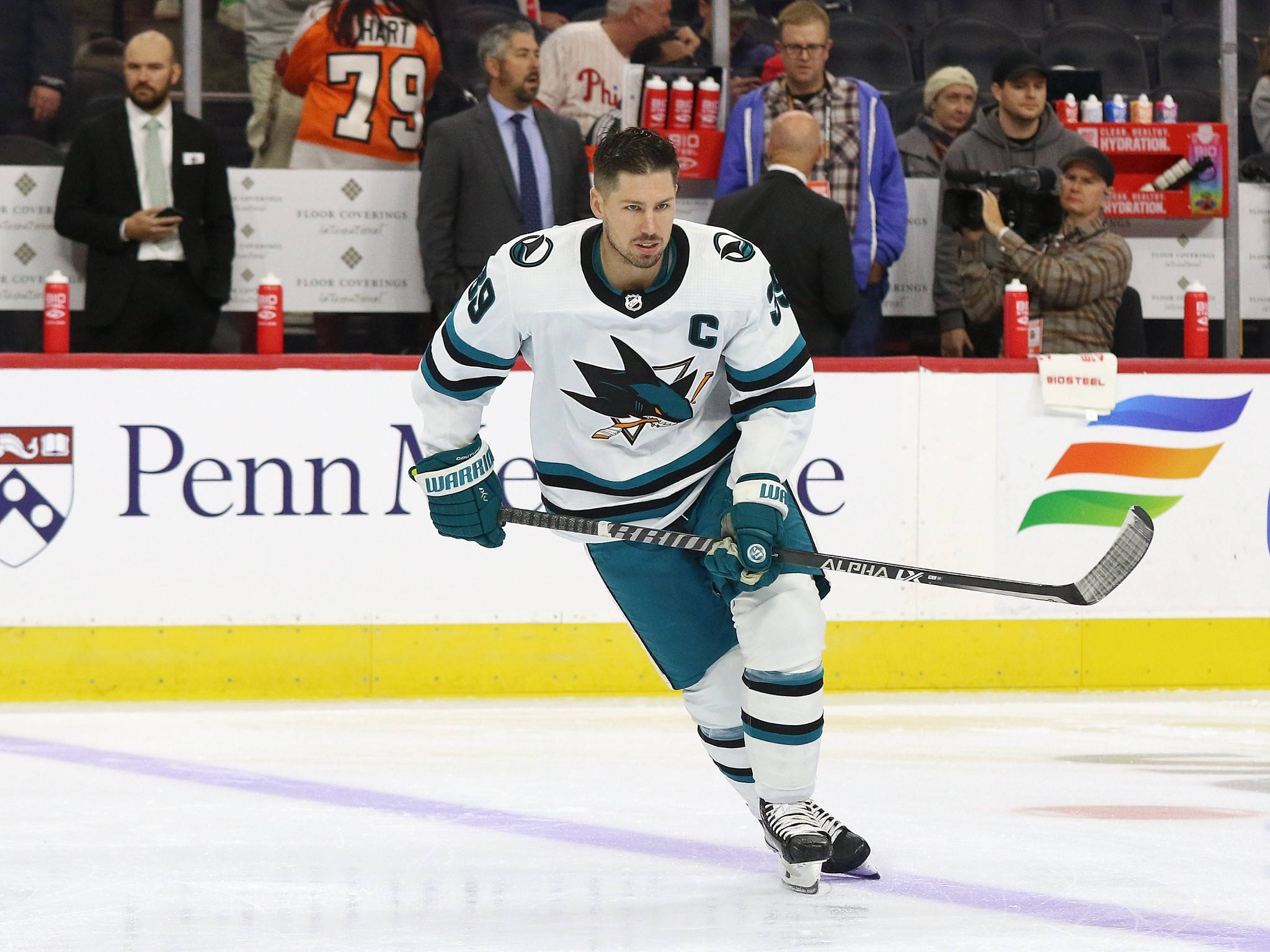 hockey 桌布 壁紙 — 一位聖荷西鯊魚隊的冰球運動員，身穿白色和青綠色的球衣，在比賽中專注地向前滑冰。