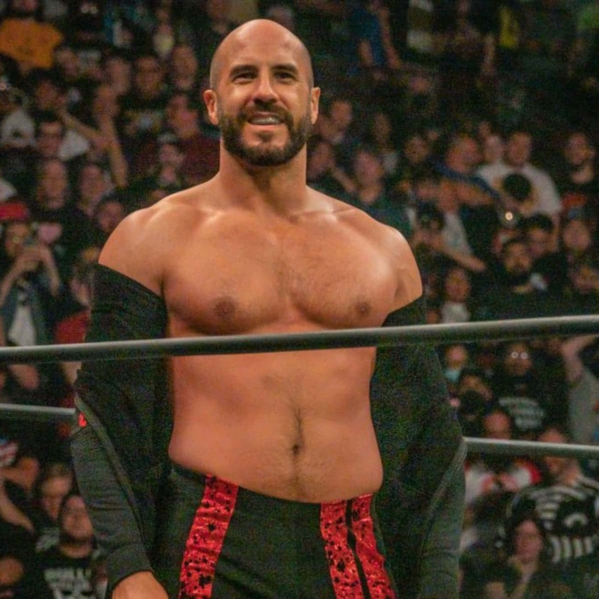 Aew 桌布 壁紙 — 一位肌肉發達、光頭、留鬍子的摔角手在擂台上自信地微笑，身後人群歡呼。